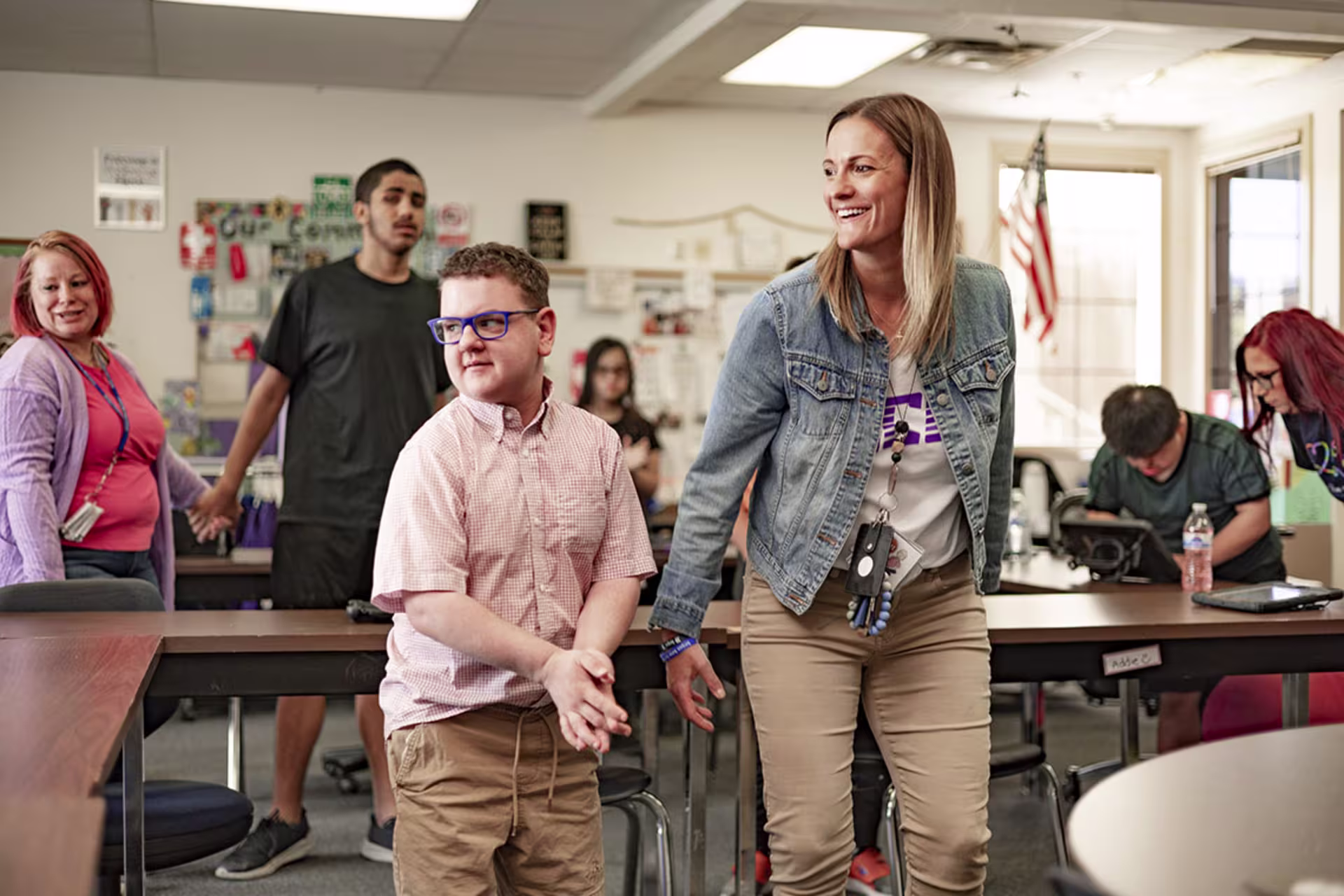 Focused shot of female special education teacher with male student next to her and other educators and students behind them