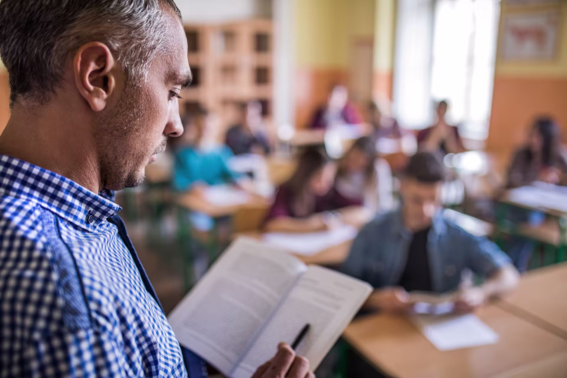 Male English teacher teaching from book to class