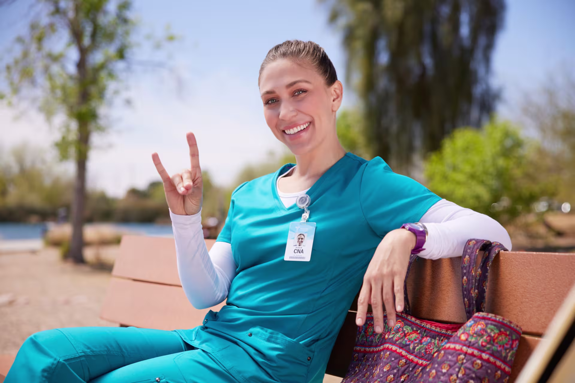 A nursing student in teal scrubs smiling and making a Lopes Up gesture outdoors, representing getting started with the Post-MSN Nursing Certificate program.