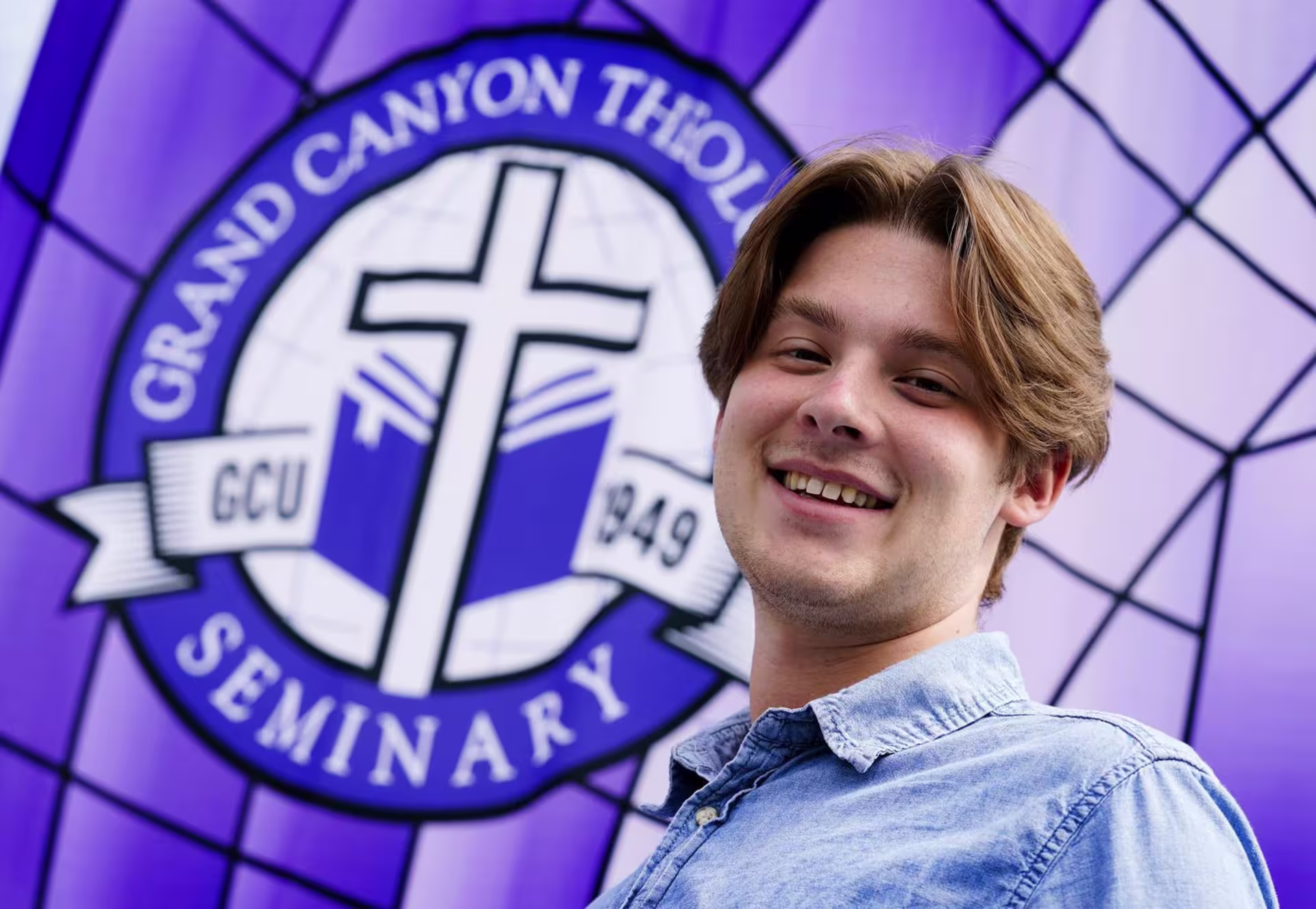A male College of Theology student standing in front of the GCU Theological Seminary sign.