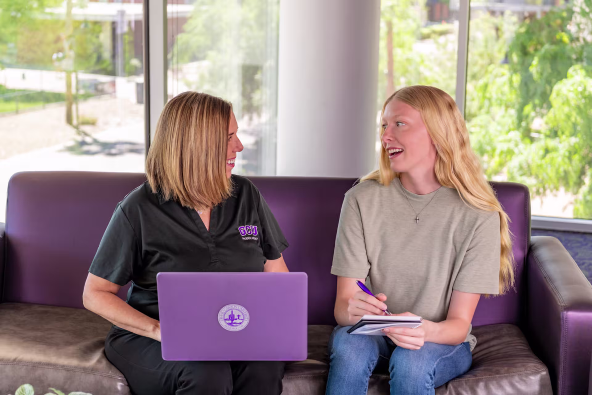 School counselor sitting on a couch with a laptop while talking to a student