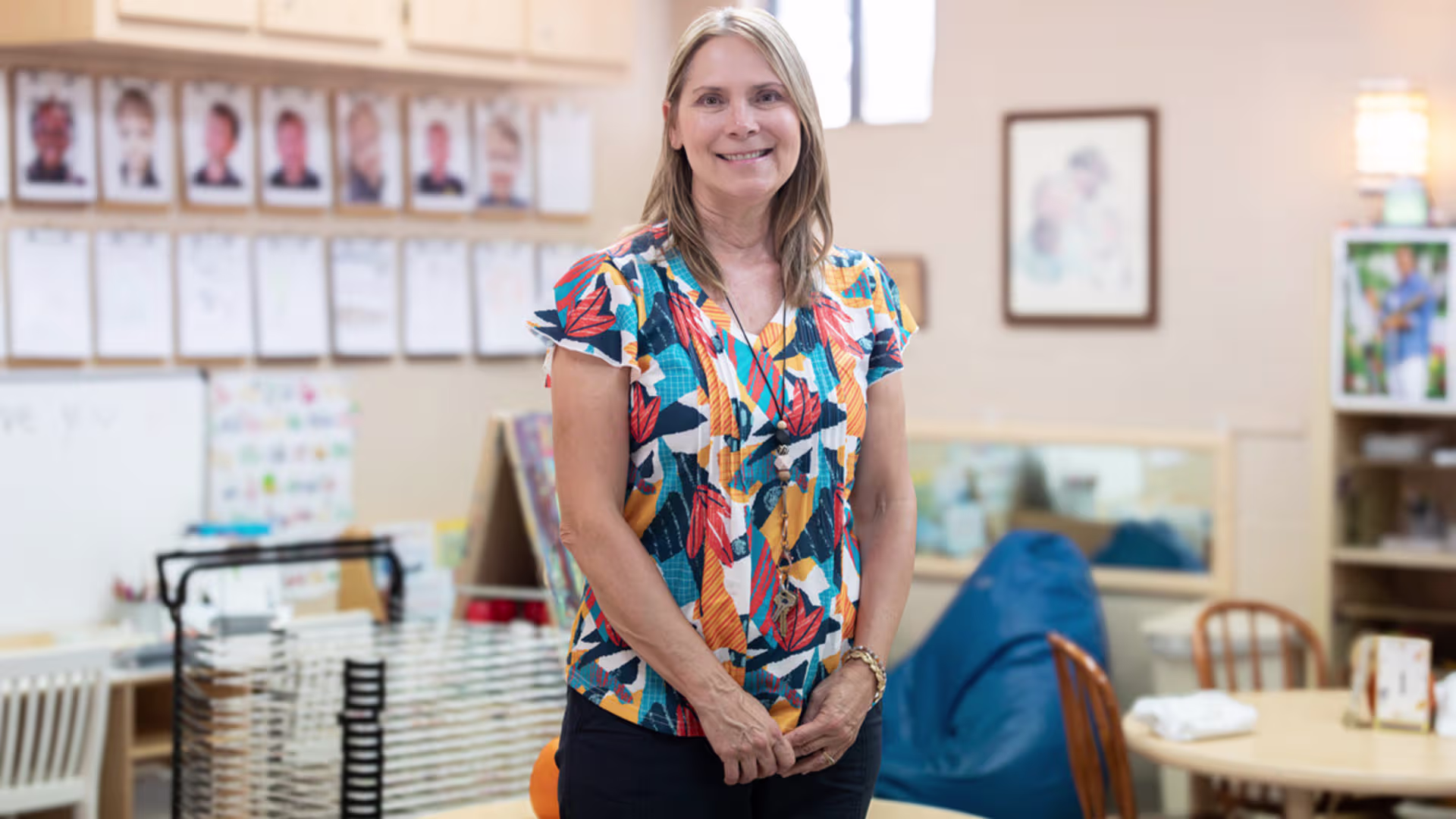 early elementary teacher in a colorful shirt stands in a classroom