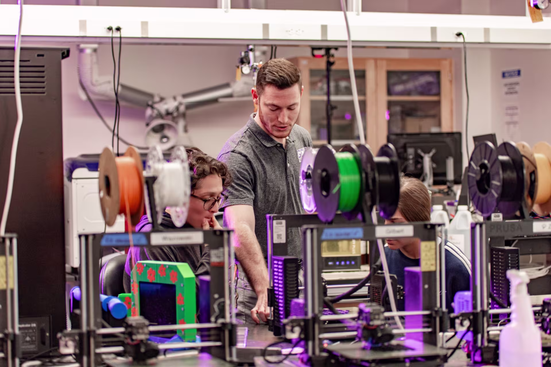 male engineering teacher talks to two in 3d mechanical printing lab