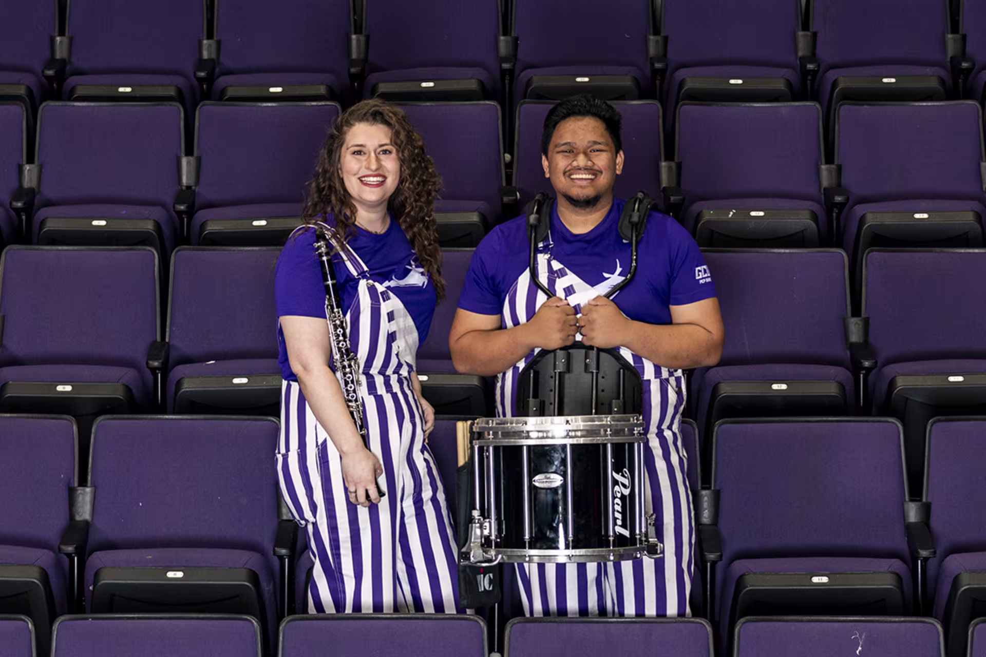 Female and male pep band students smiling in stands while holding their instruments