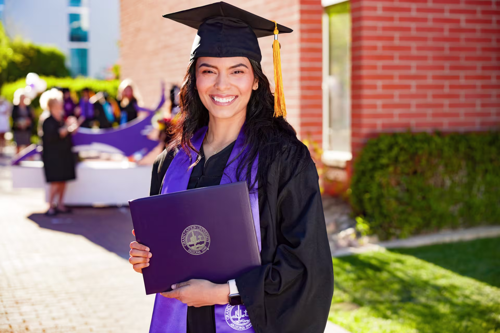 Headshot of female graduate outside in cap and gown holding diploma