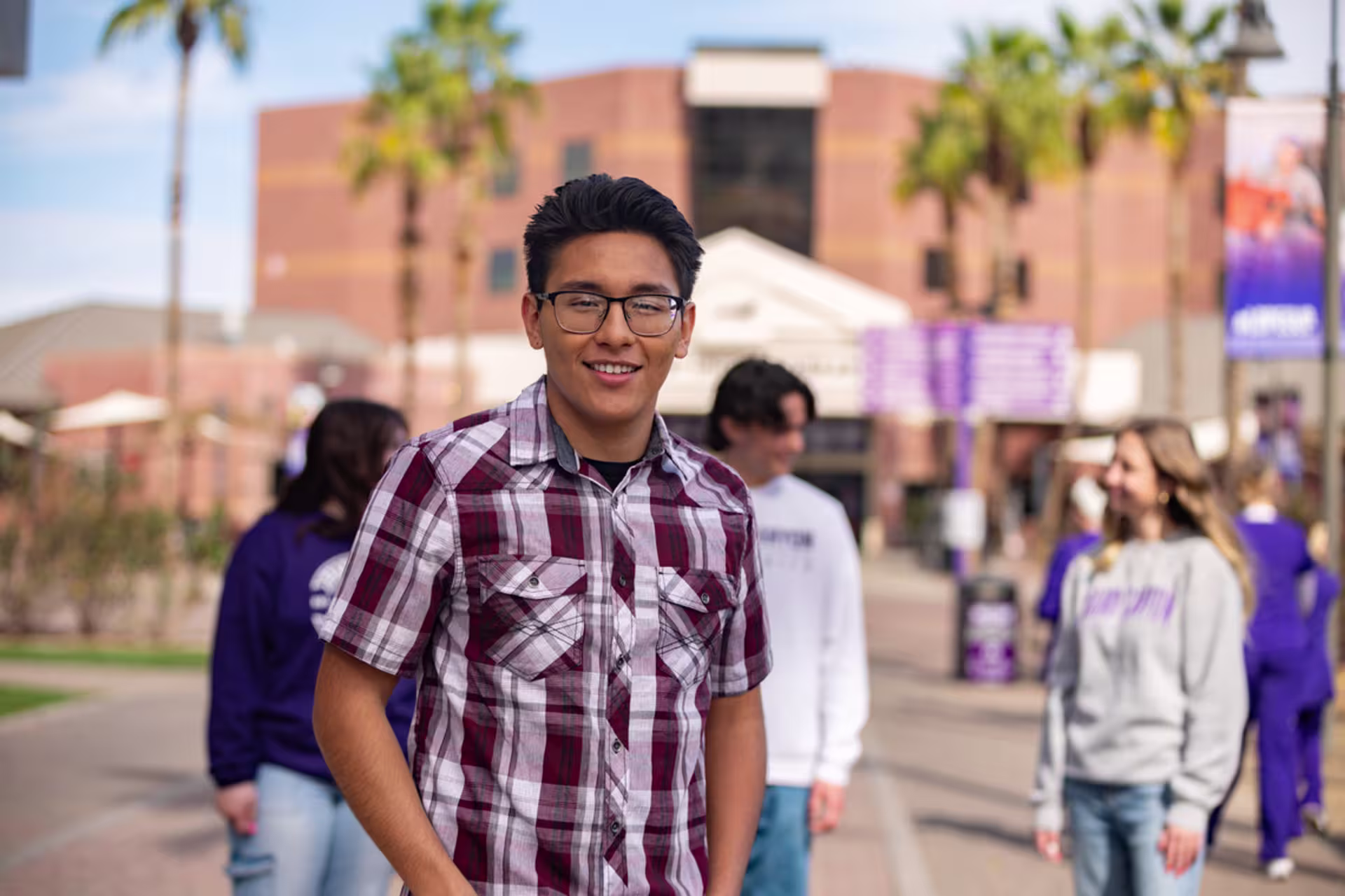 hispanic male with black glasses in plaid shirt in busy gcu walkway
