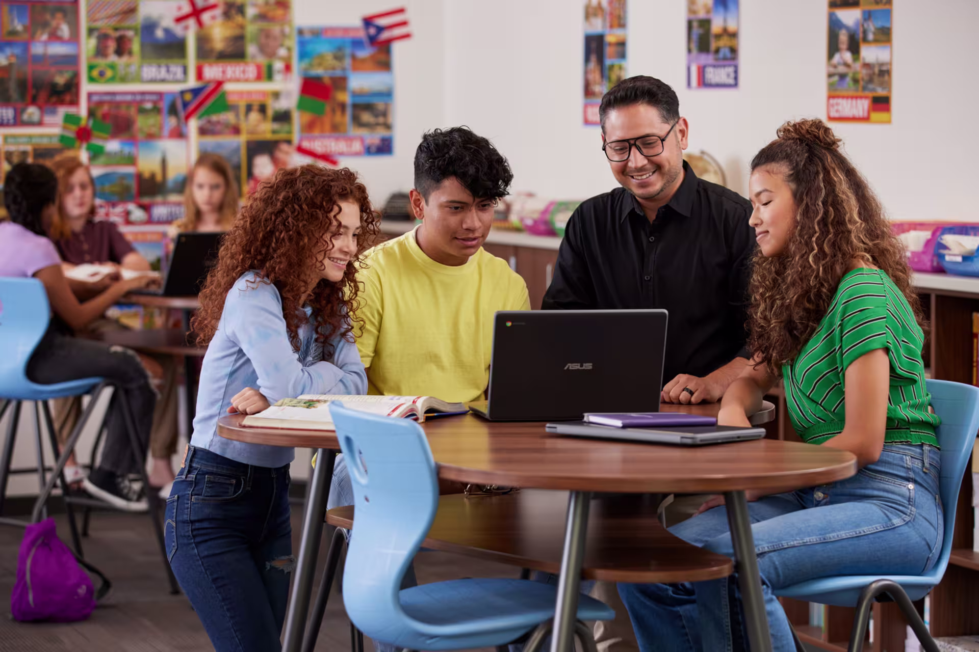 Male high school teacher working on laptop with three students at desk