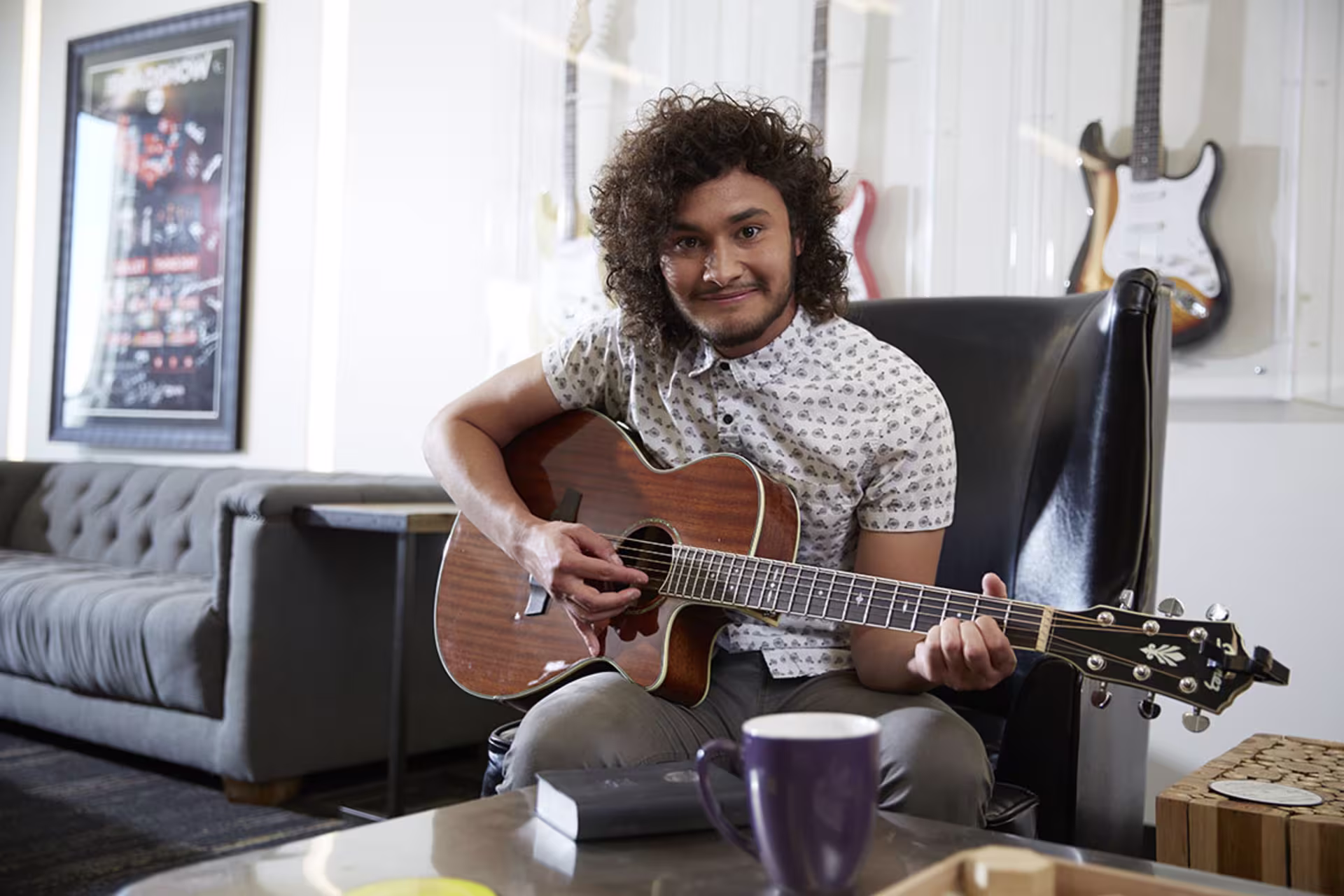 Male music student sitting down, holding guitar, and smiling at camera