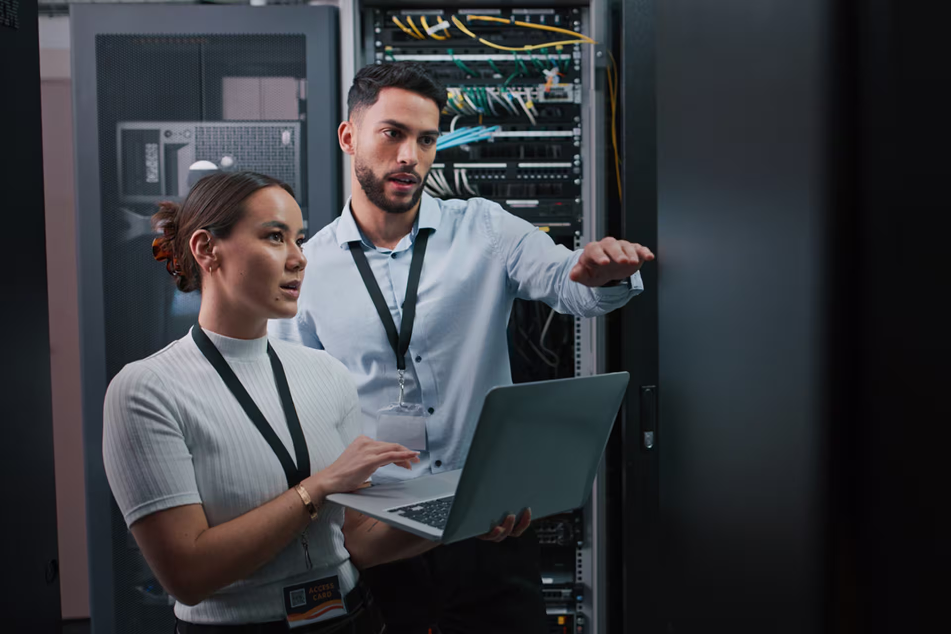 woman uses laptop in server room while guy explains something ahead