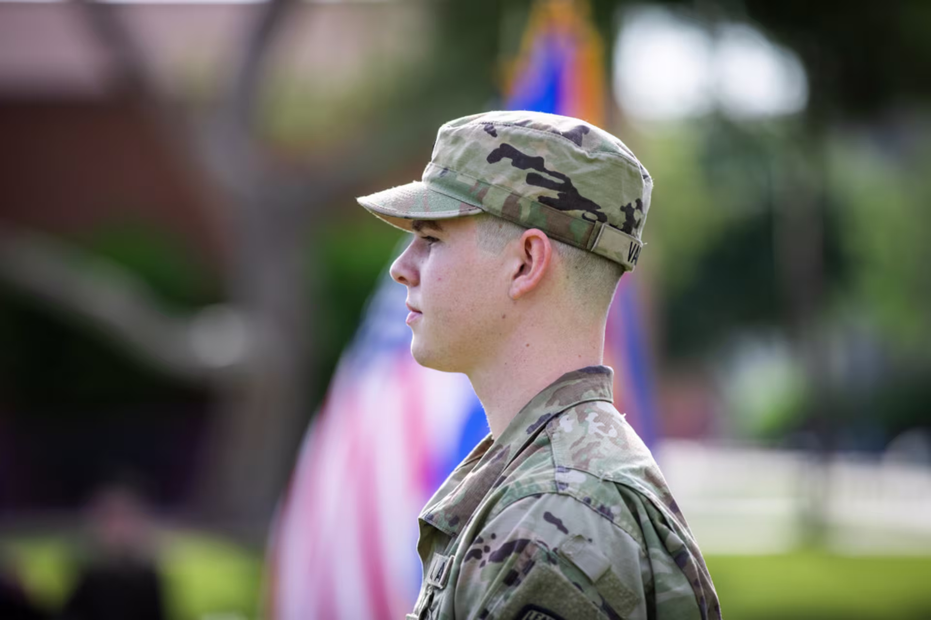 Side view of soldier standing in a military uniform with an American flag in the background