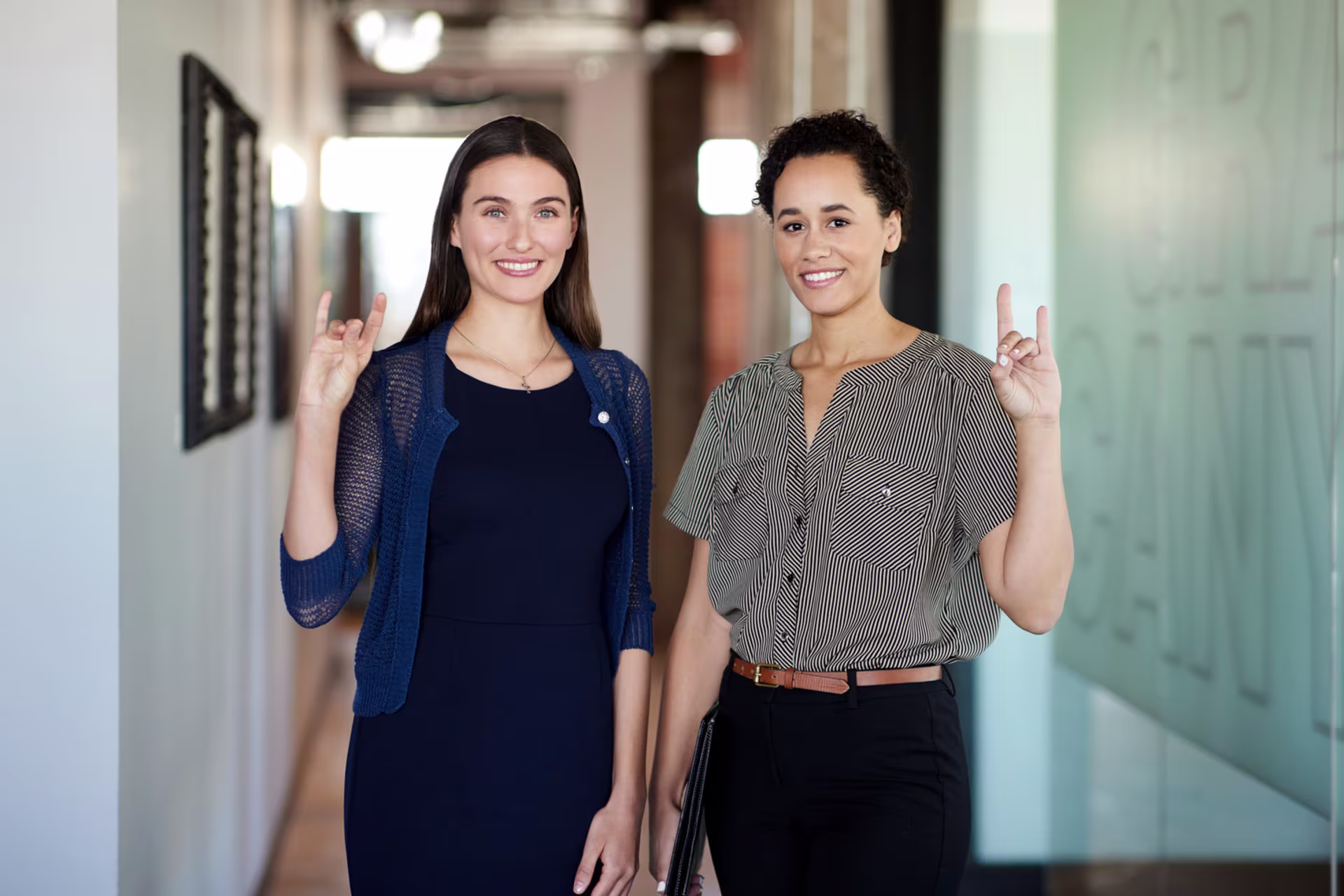 Two women smiling in office hallway holding Lopes Up hand sign