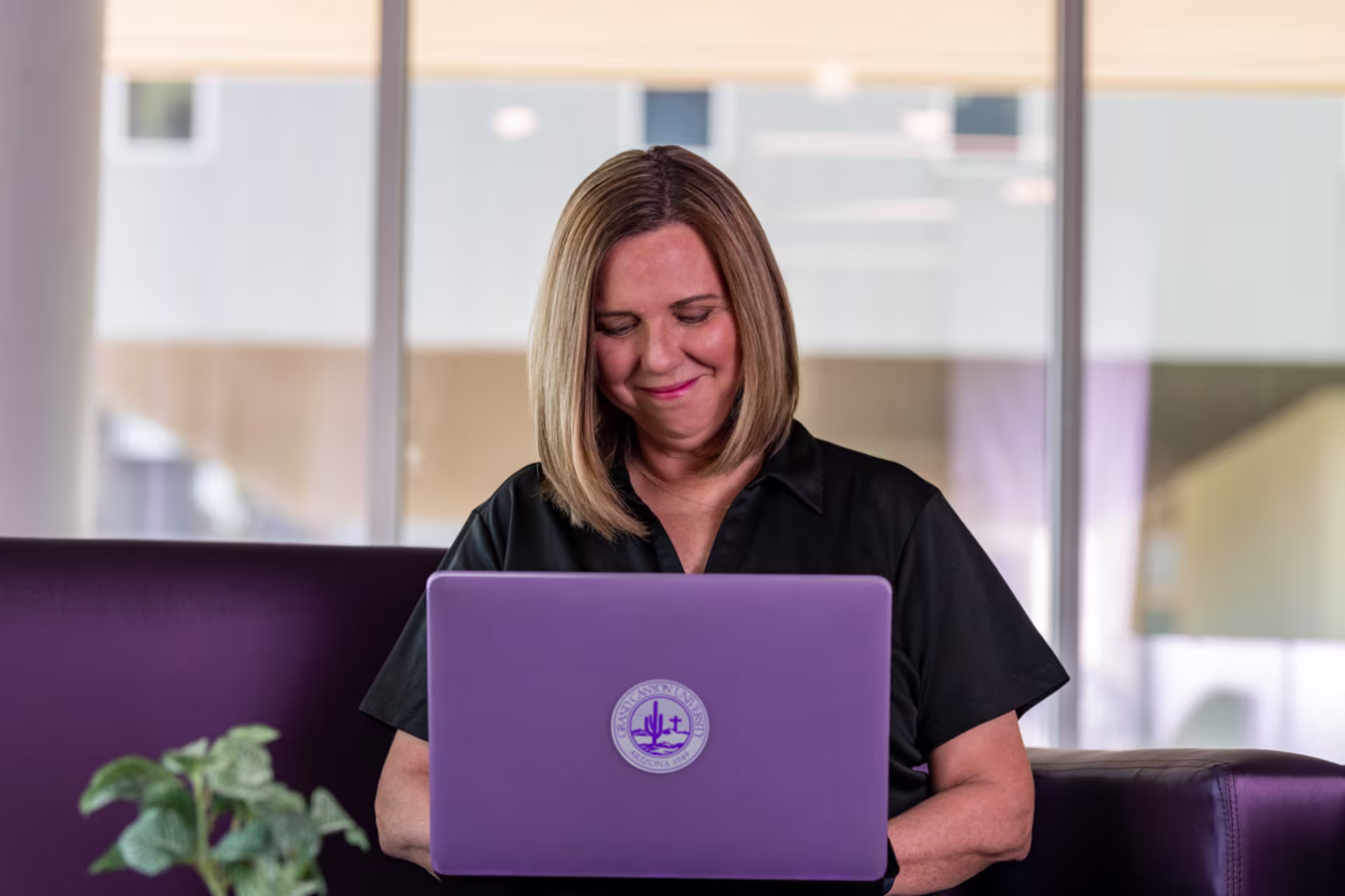 Woman sitting at a desk with a laptop with a purple case in an office setting