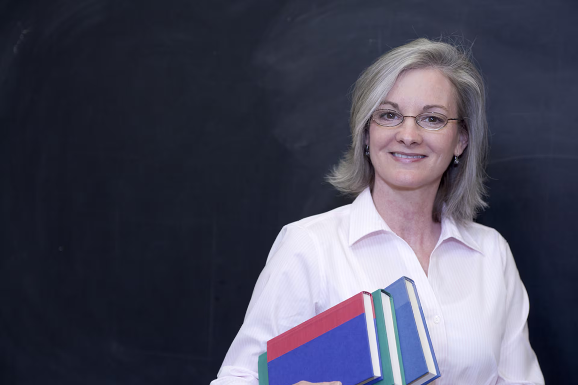 older woman in a white collared button-down shirt holds bibles under arm