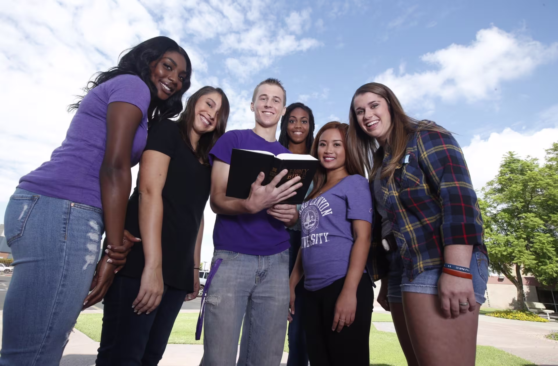 Six students standing outside reading bible