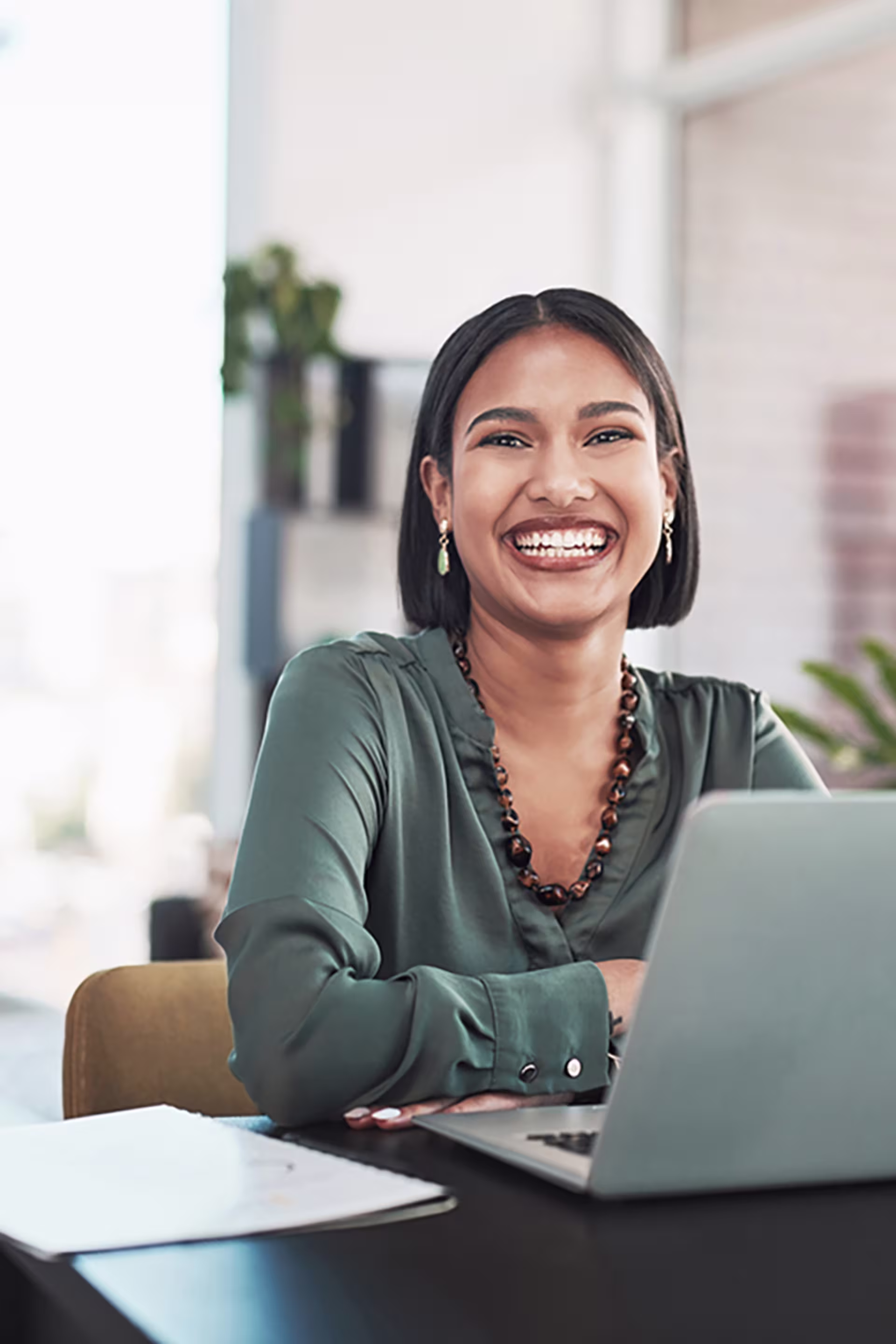 black woman with bob haircut smiles while working on online coursework on a gray laptop