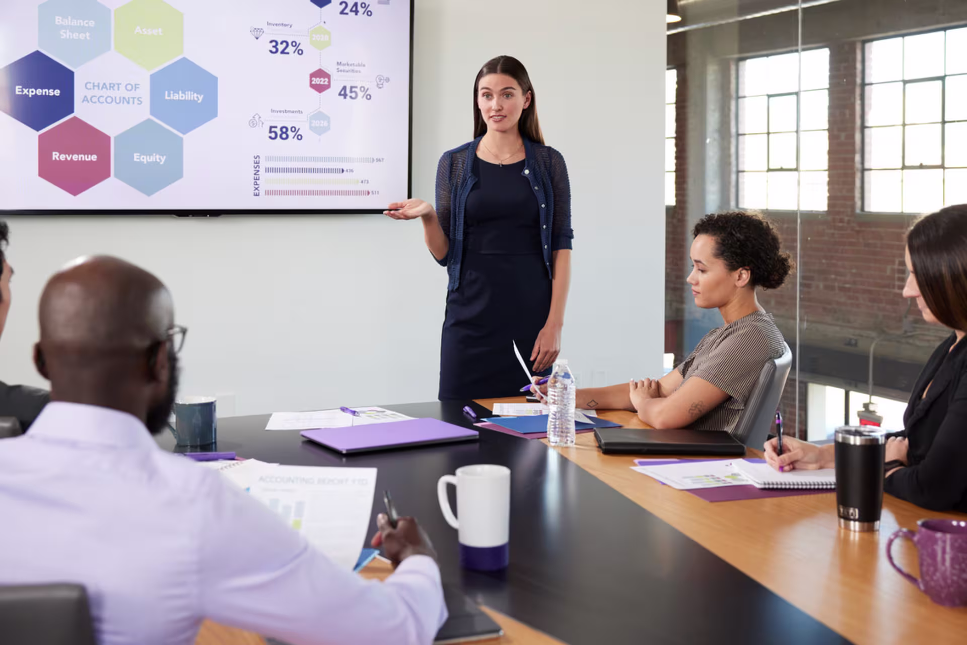 female accounting student standing in front of a presentation and talking to peers in a corporate environment