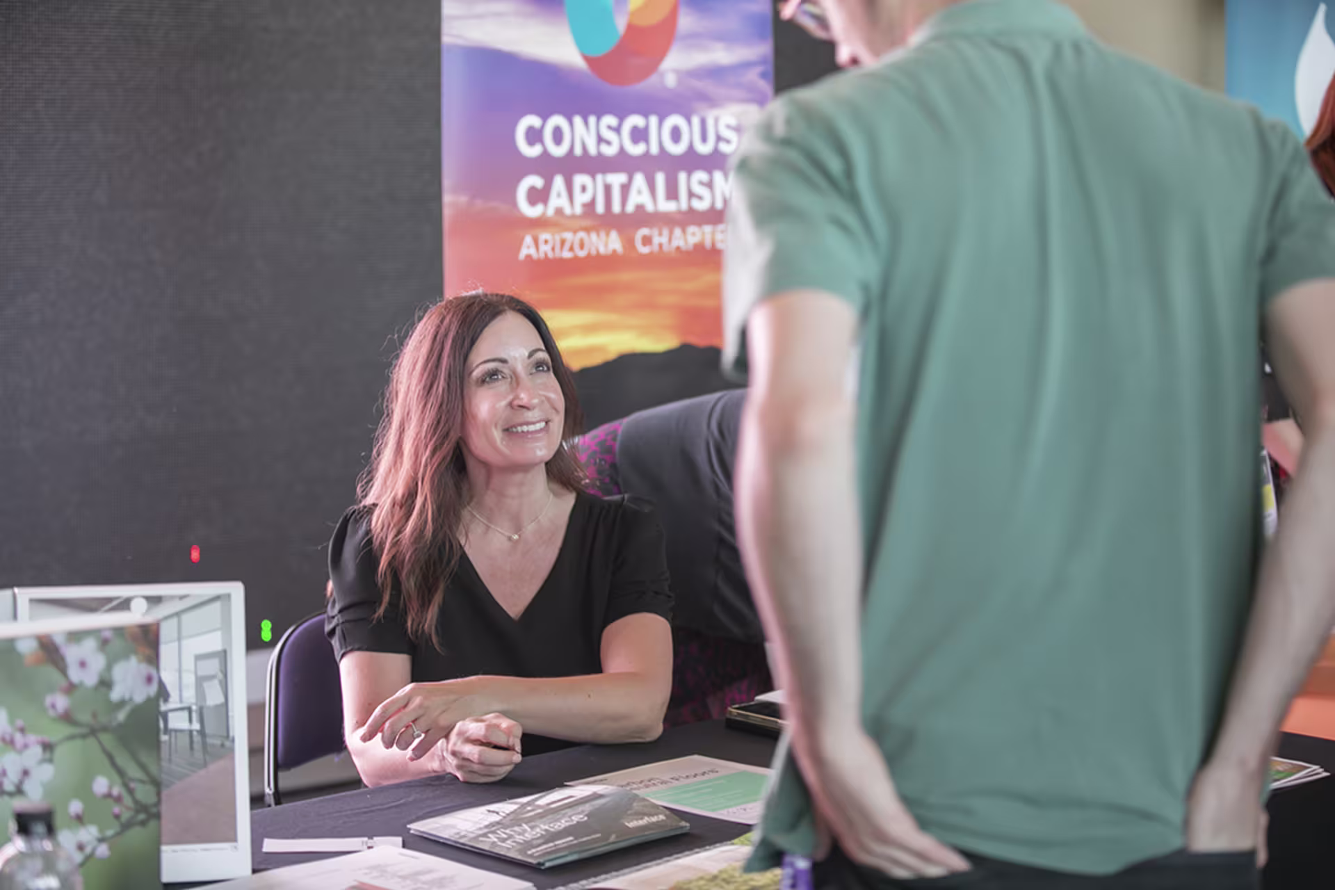 Female business professional sitting at Conscious Capitalism booth and talking to male student at a Beyond Zero Event