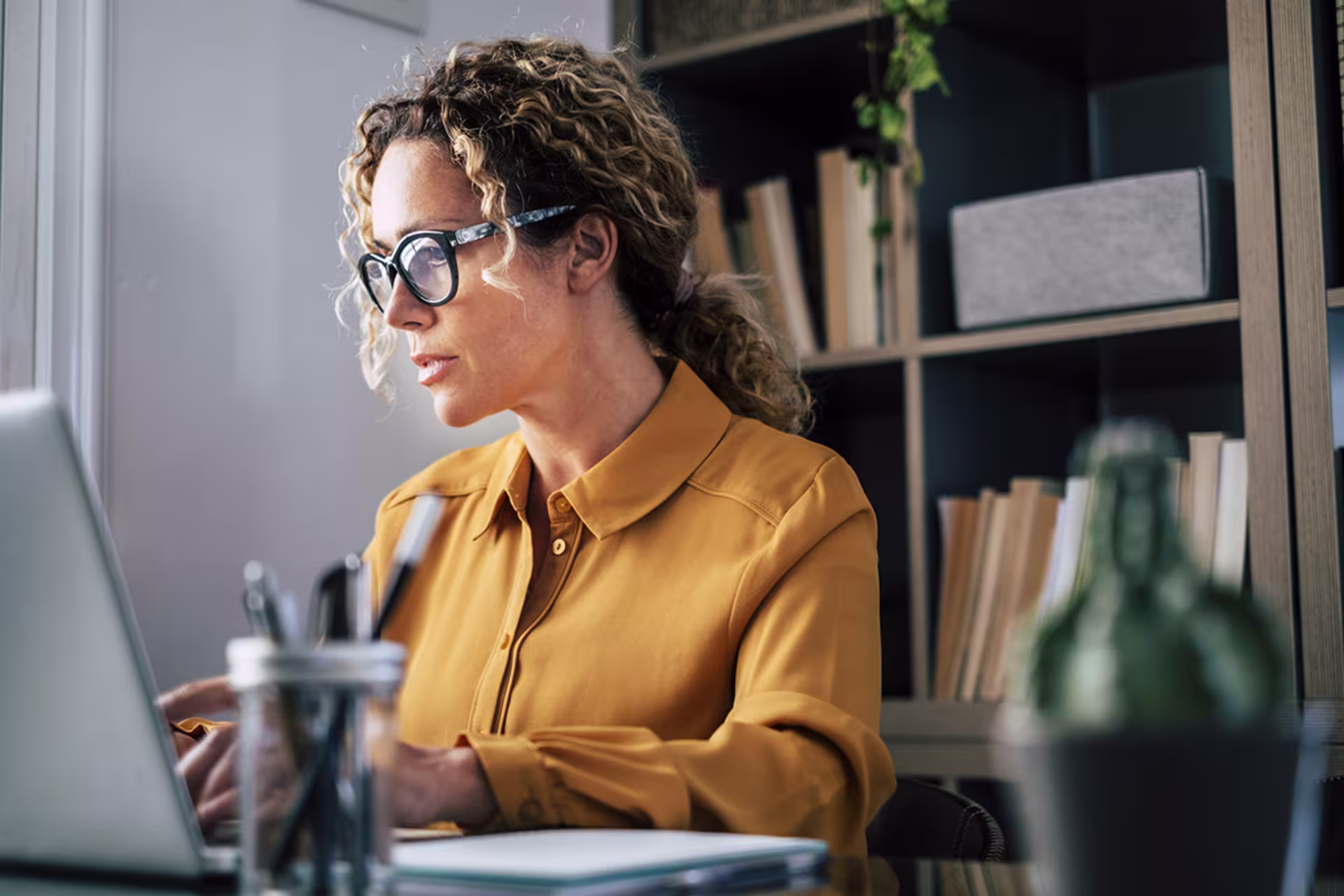 focused businesswoman with curly hair pulled back in gold shirt types on laptop for doctoral class