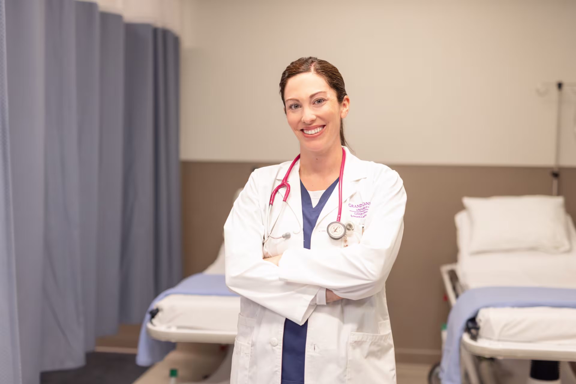 A female healthcare manager wearing white coat and smiling with arms crossed in hospital setting.