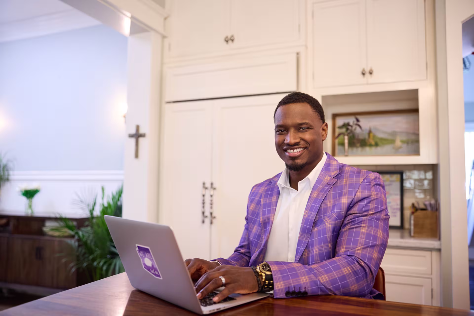 A male smiling while studying healthcare management on his laptop in the kitchen.