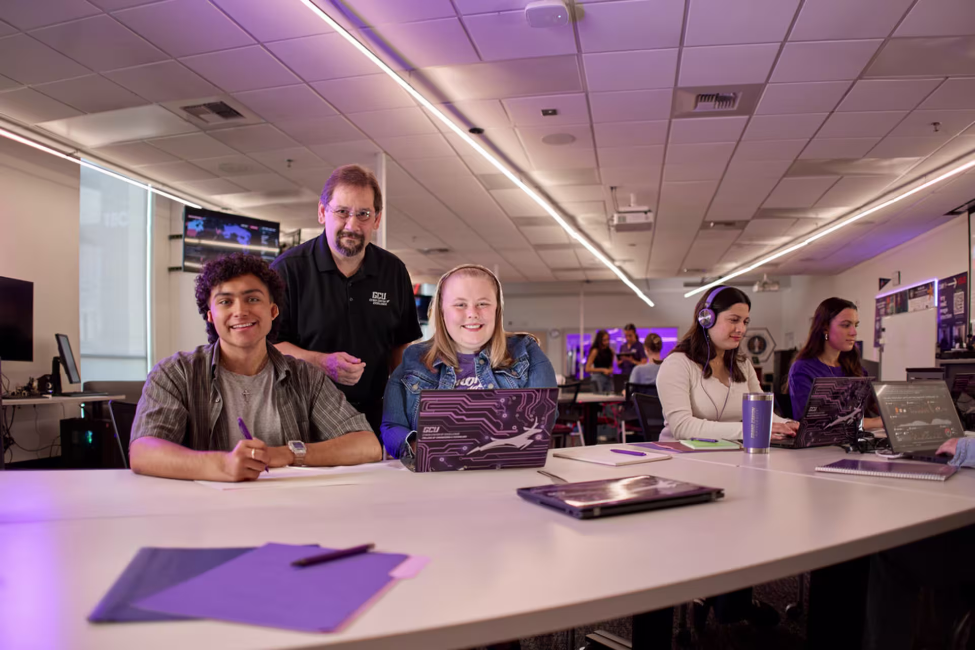 Software development students sitting in a class setting and smiling with laptops