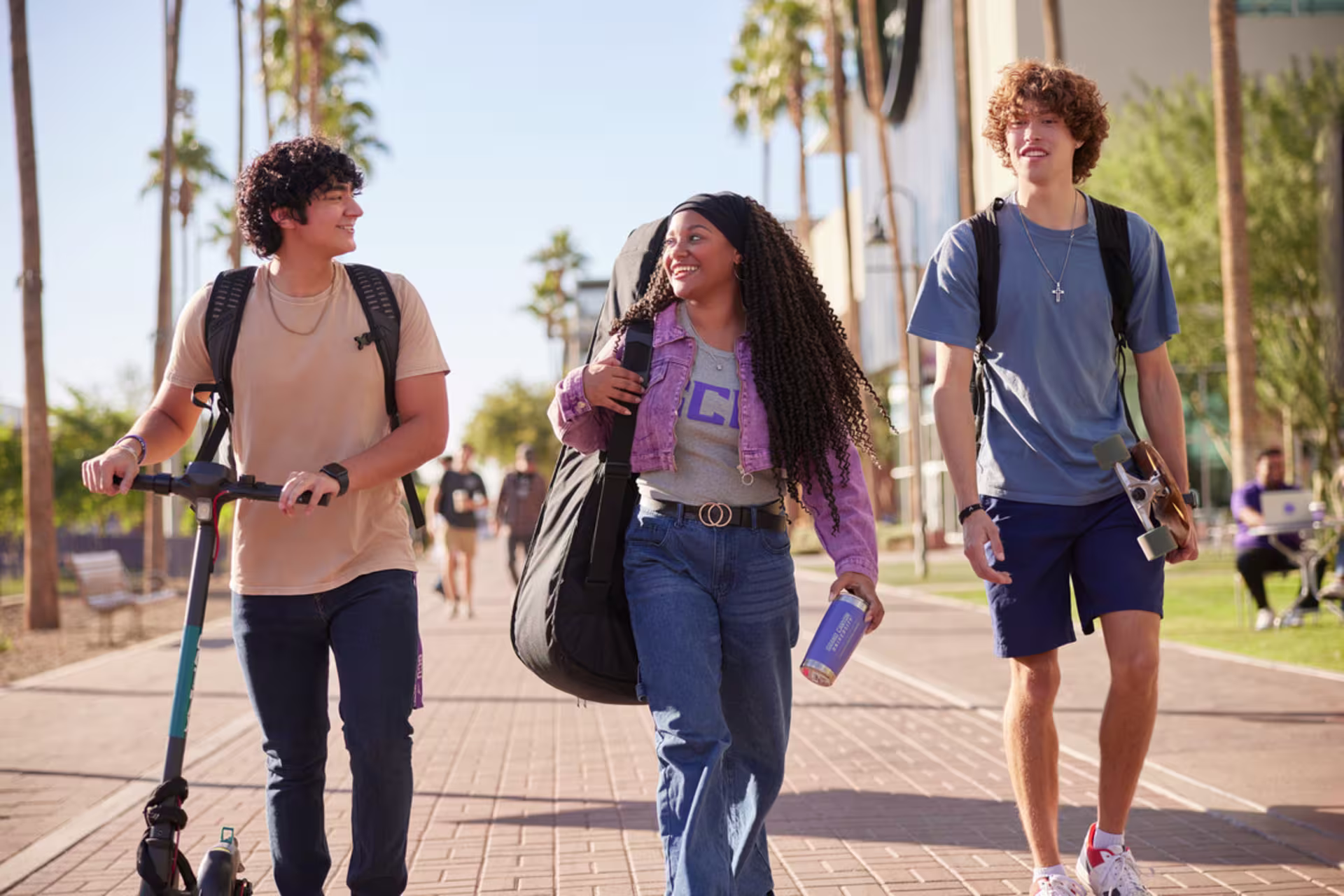 black girl with instrument case walks on GCU campus next to hispanic and white male campus students with an e-scooter