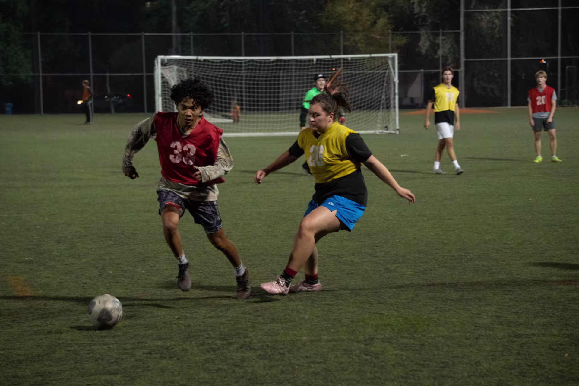 girl in yellow jersey races up to steal the soccer ball from male player in a red jersey during a coed intramural sport game