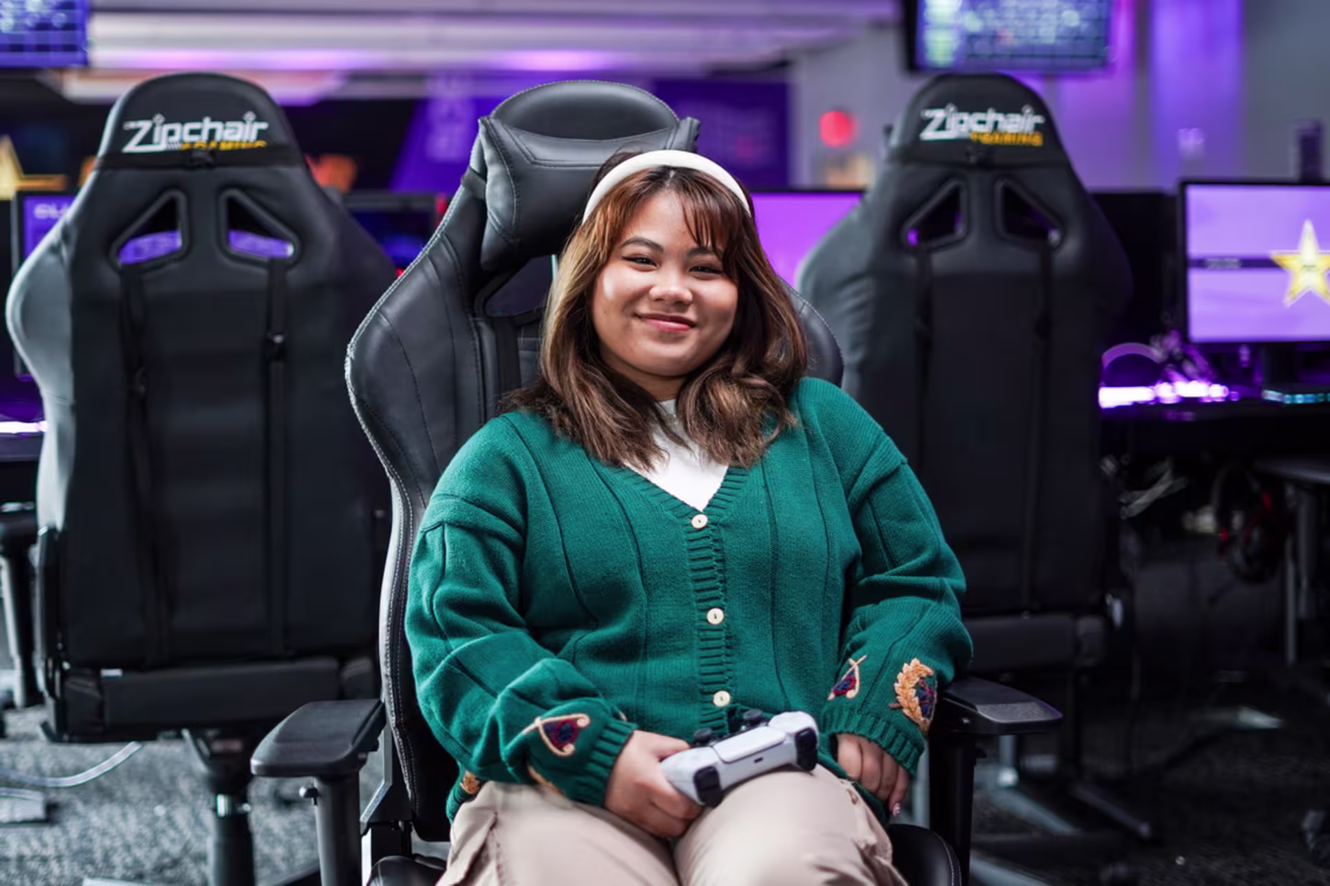 female Asian game developer student sitting in gaming chair in the GCU esports room holding a controller