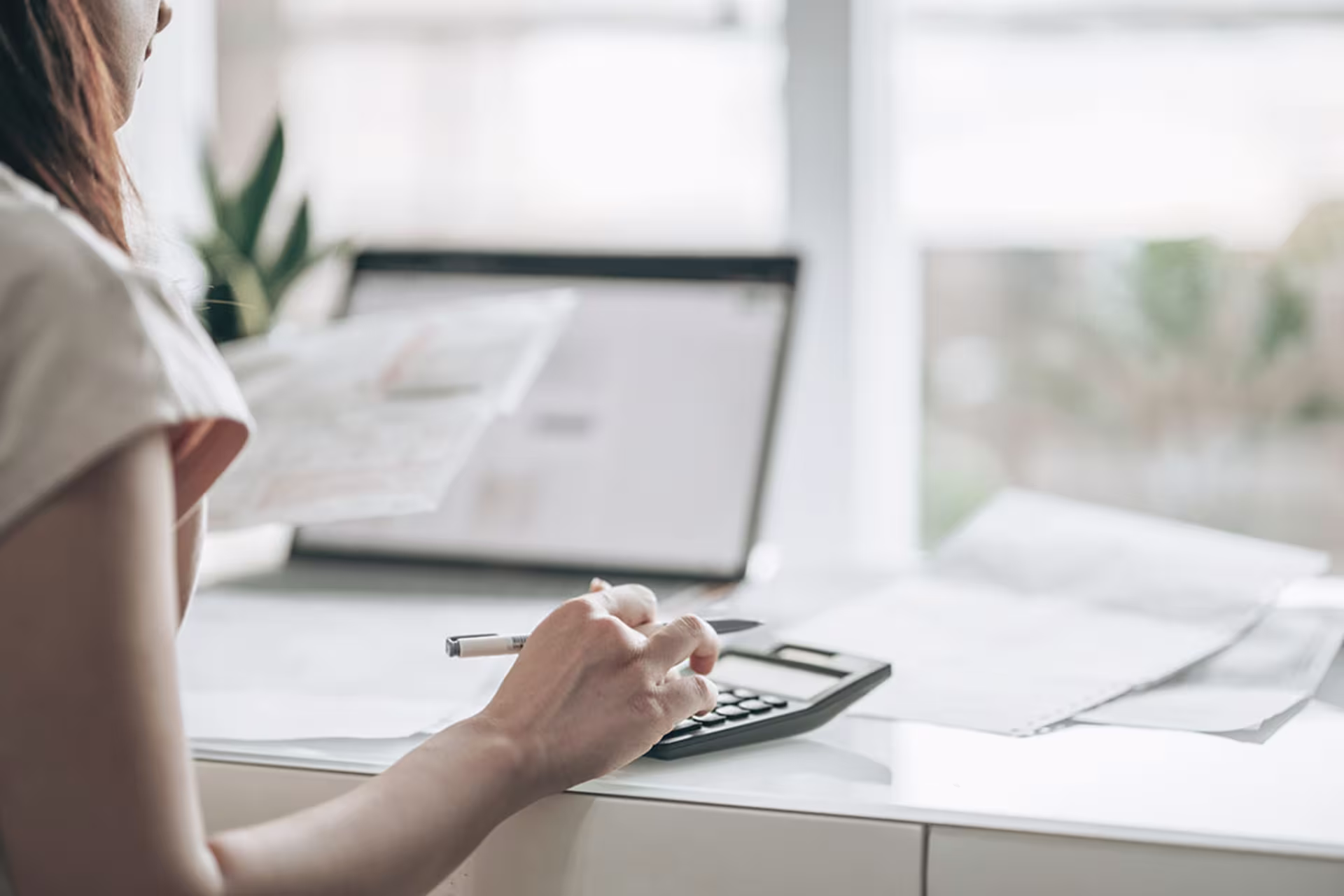 Female working on tax paperwork using laptop and calculator at desk