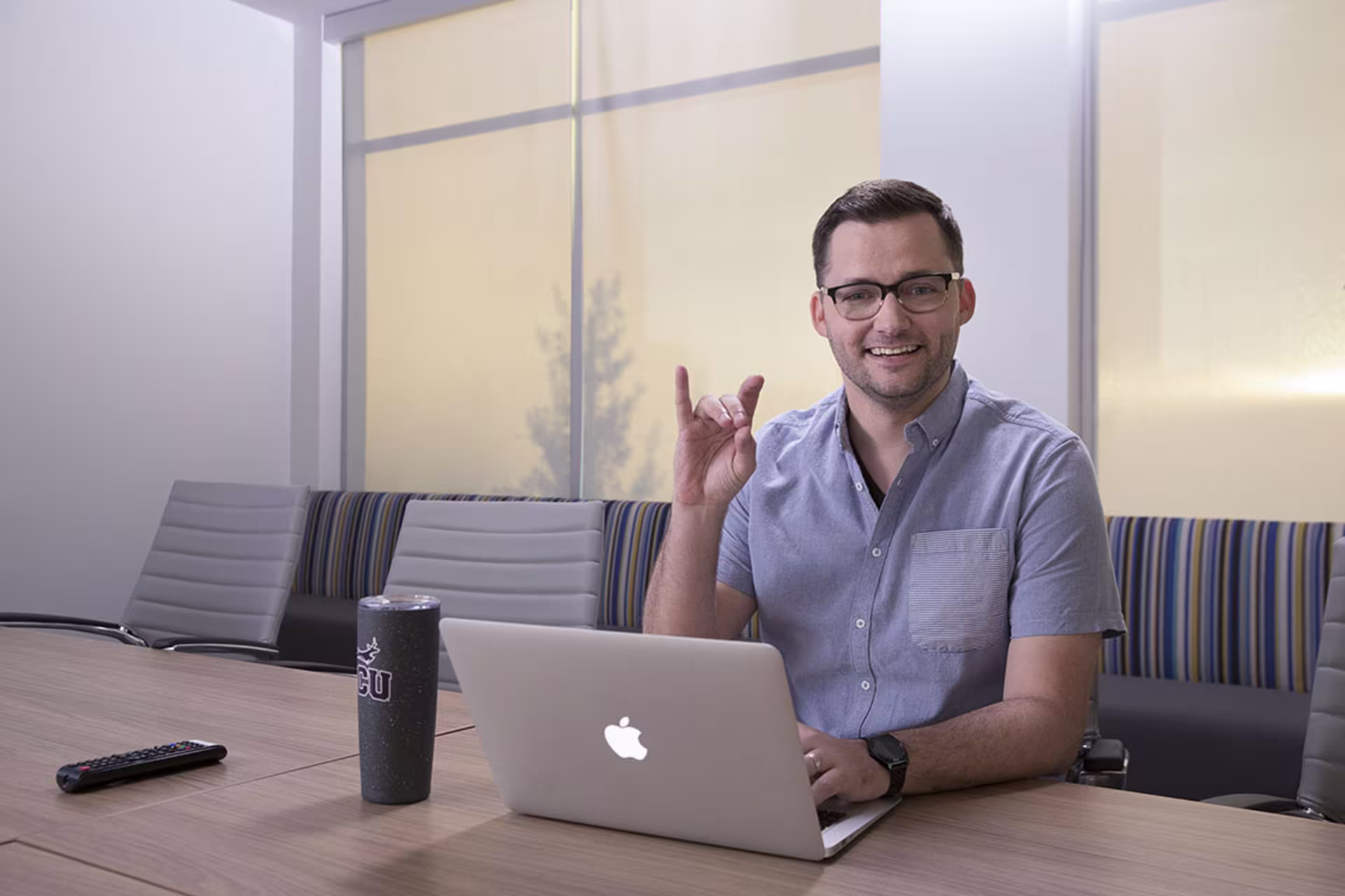 male undergraduate certificate c sharp programmer smiles with a lopes up hand sign at table with laptop open for coding