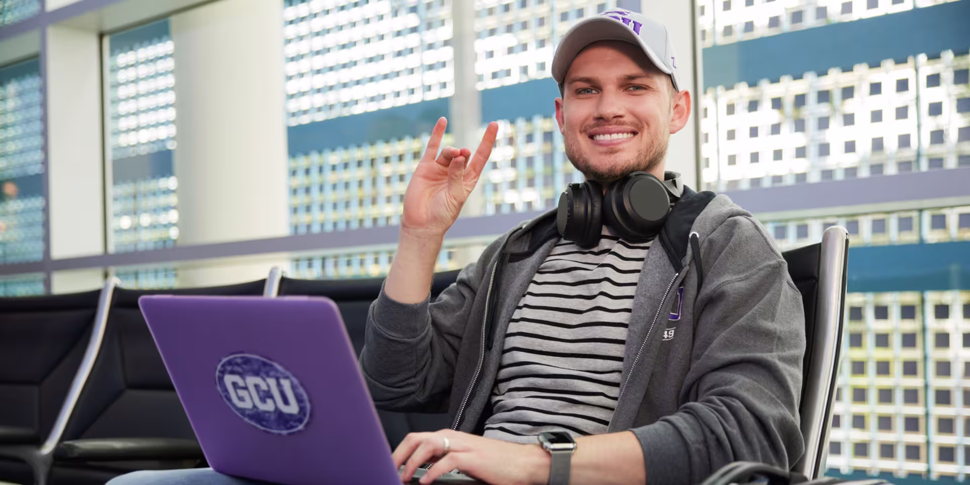 An online student smiles while holding up the Lopes Up hand sign, seated with a GCU laptop