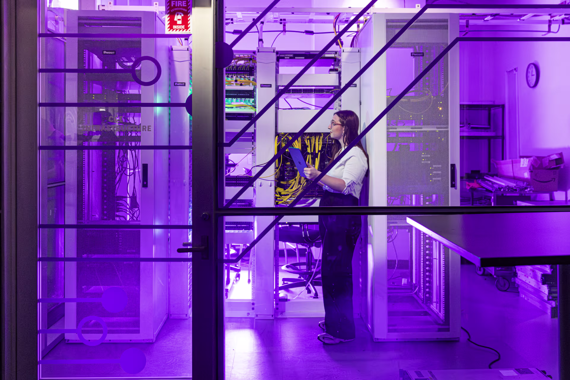 Person works with server racks in GCU’s CCE server room, lit with purple lighting and filled with networking equipment