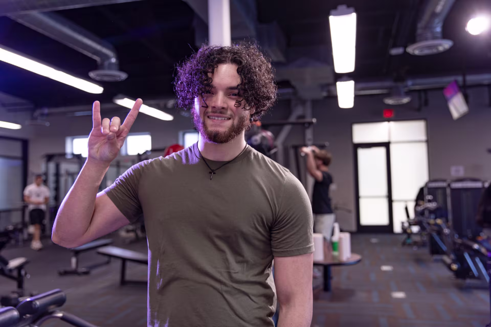 Male exercise science student gives the Lopes hand signal while standing in a gym.