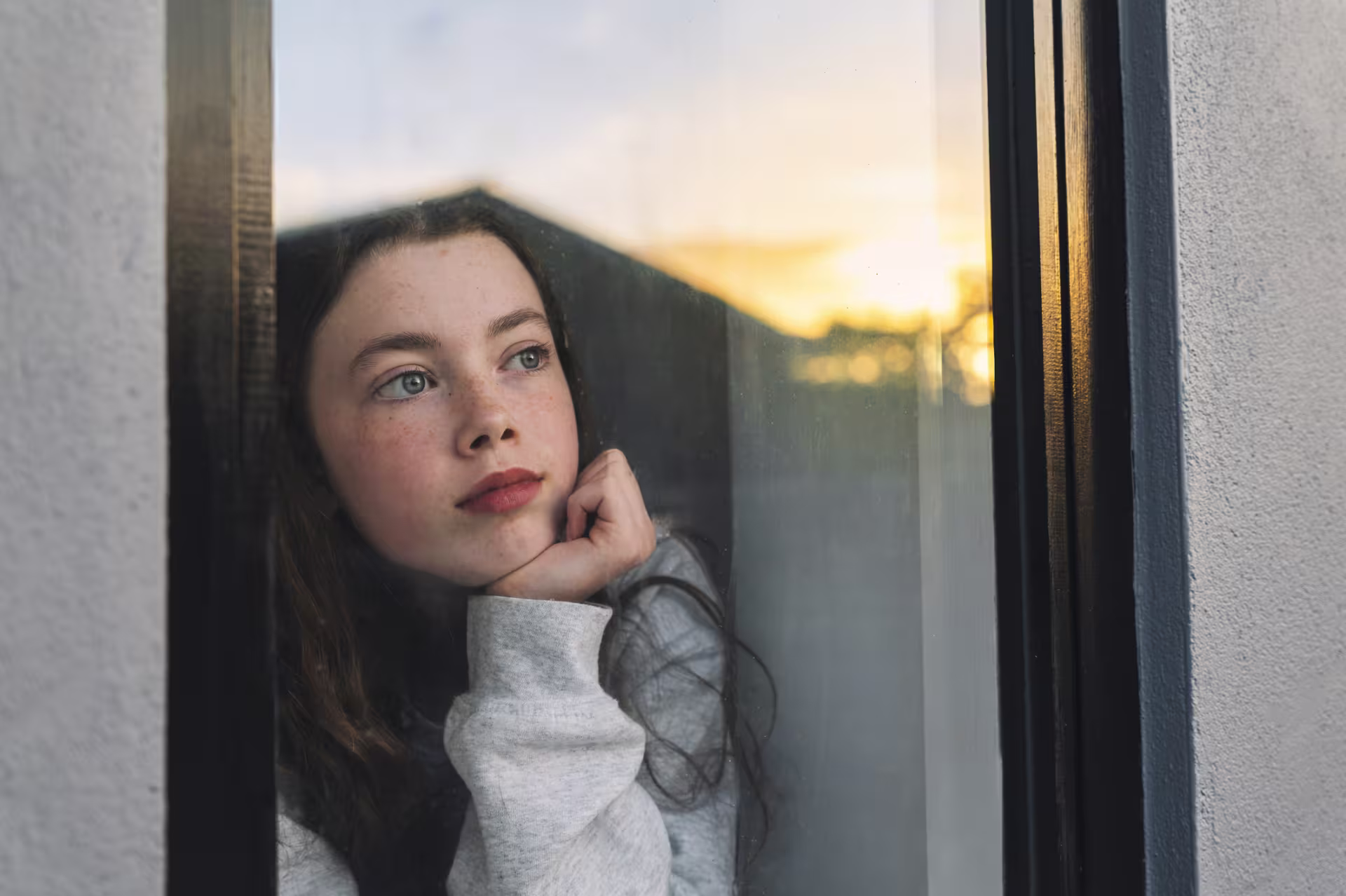 Person gazing out a window at sunset, reflecting on spiritual vulnerability and inner strength.