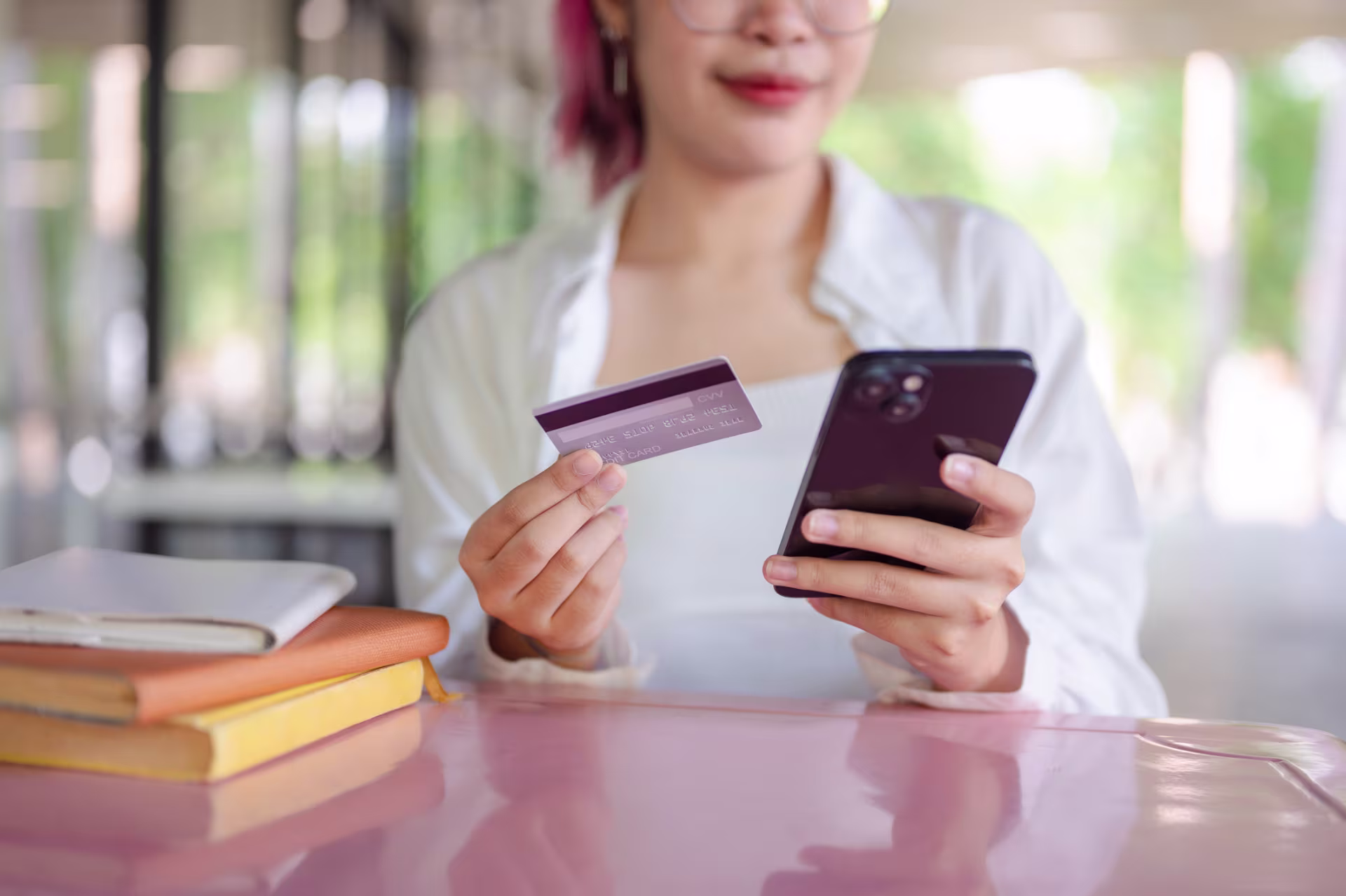 A college student with pink hair making a payment with her credit card on her phone.