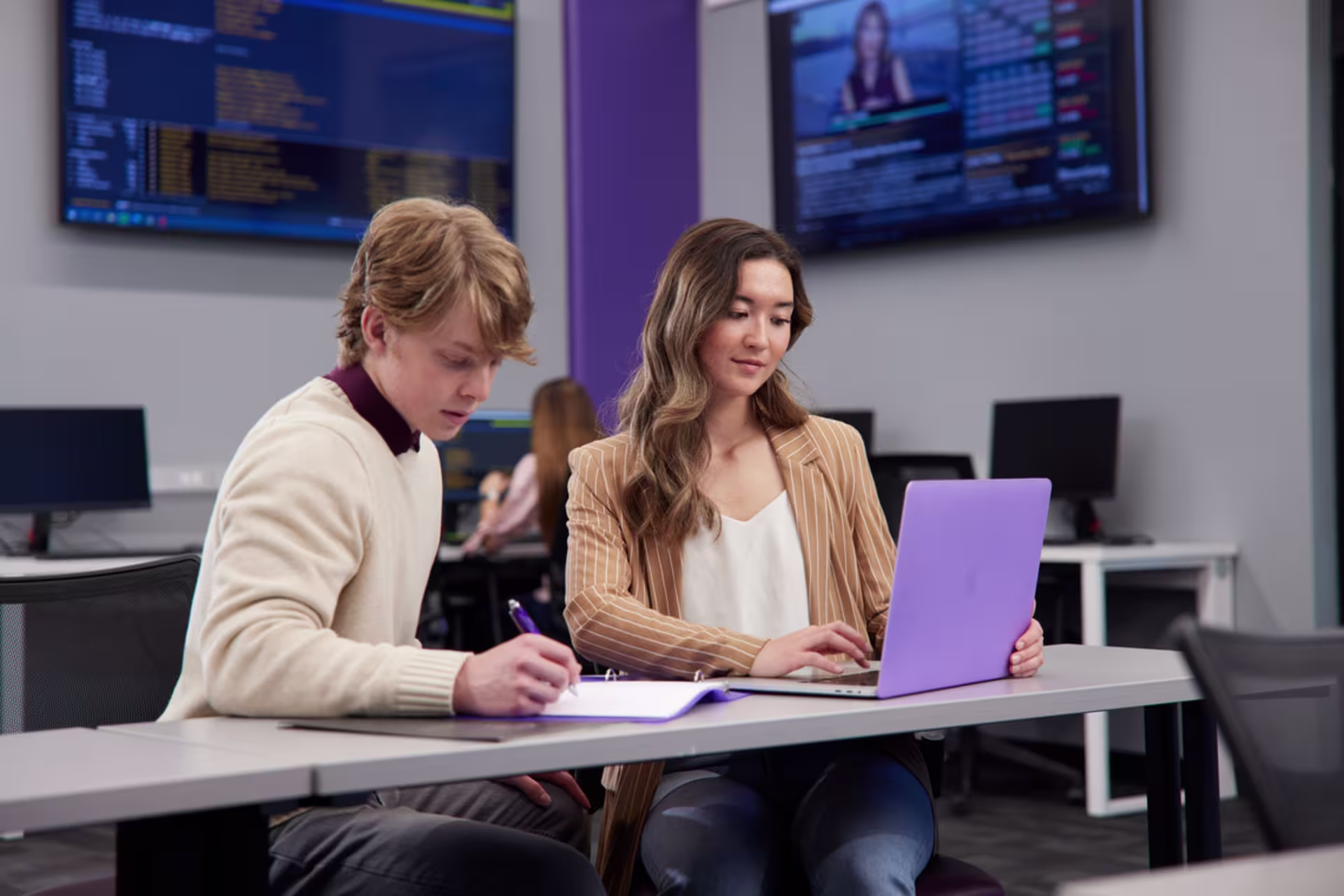 Two finance MBA students working together on laptops while sitting at a desk.