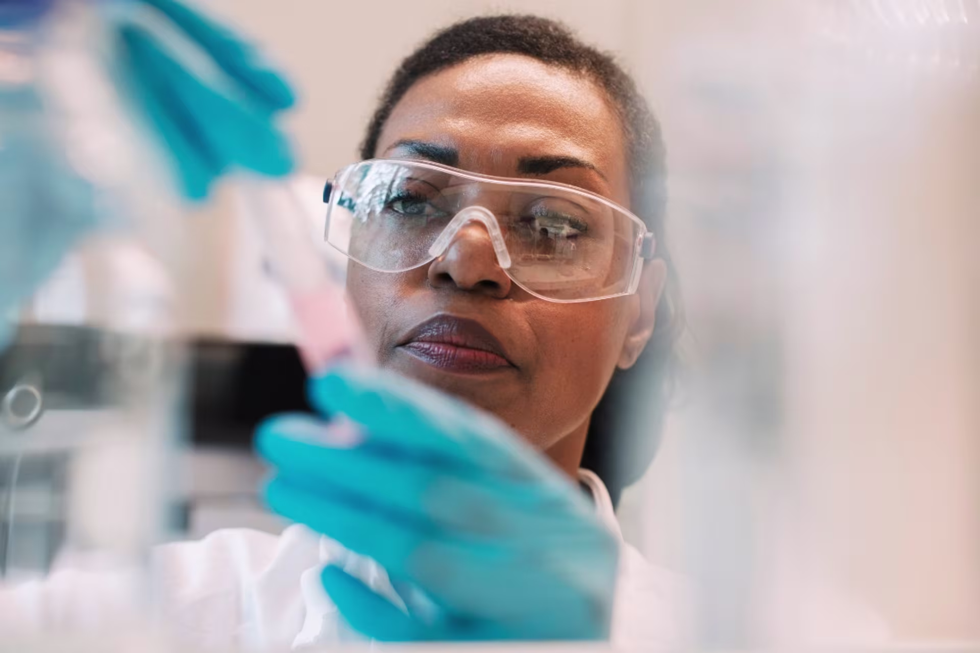 Female medical lab science students in white coat and protective glasses examining a sample in a lab.