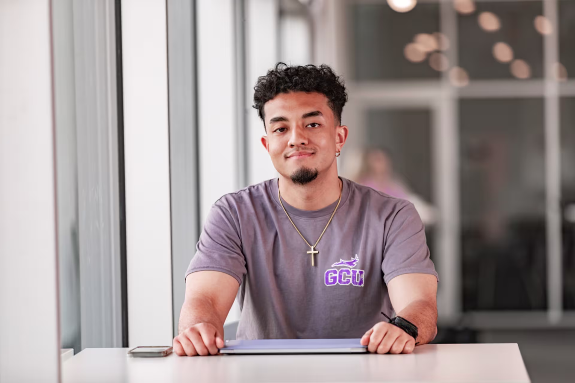 Project management MBA student in a grey t-shirt sitting at a desk with a laptop.