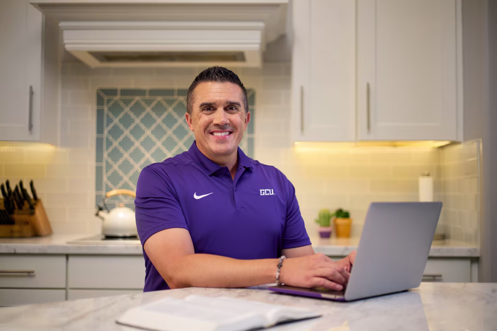 Sports Business MBA student in a purple GCU polo working on a laptop from home.