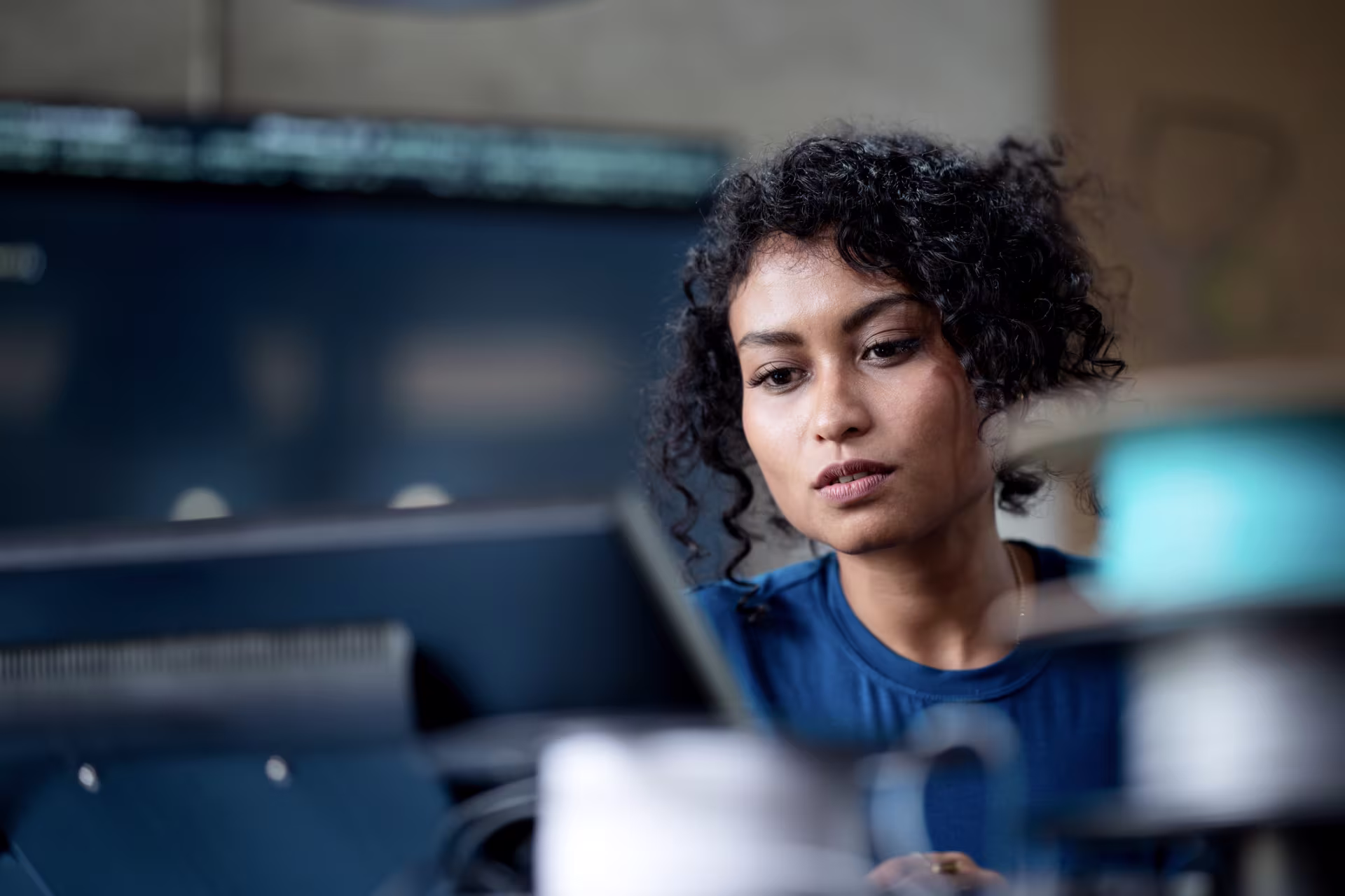 Person with curly hair sits in front of computer monitors.