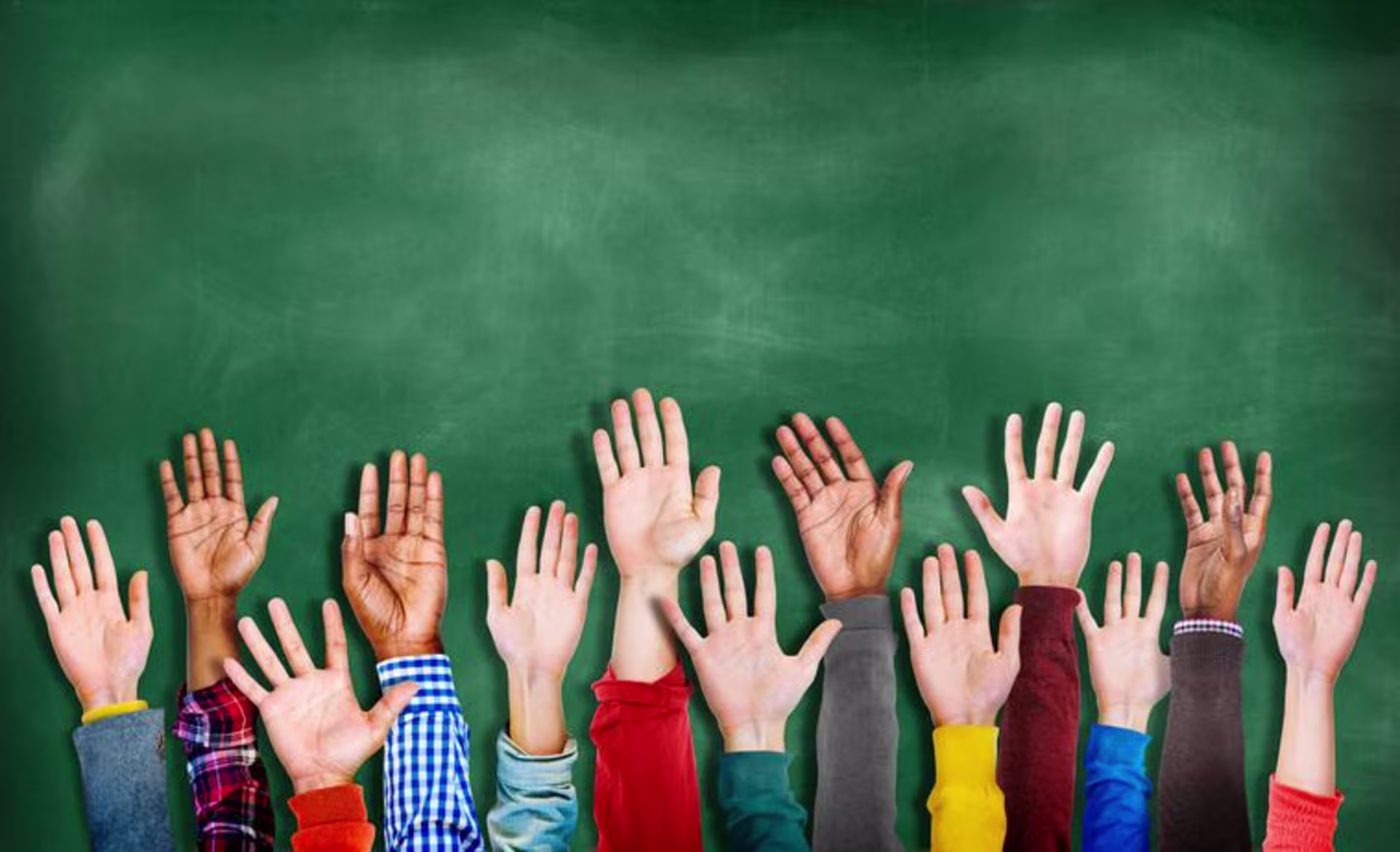 group of children raising hands in front of chalkboard