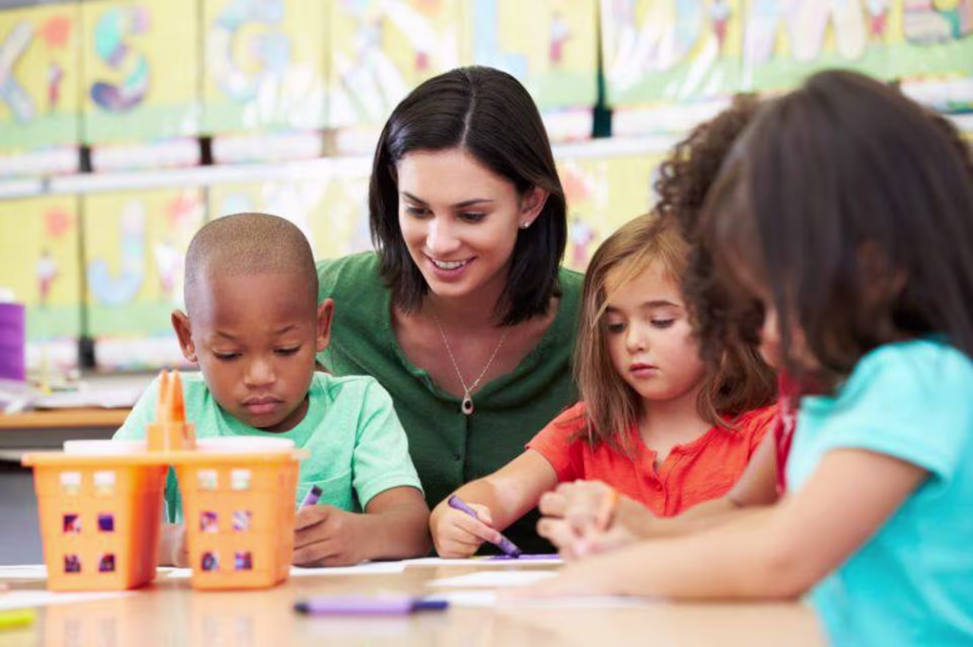 Elementary art teacher observes three kids coloring at a table