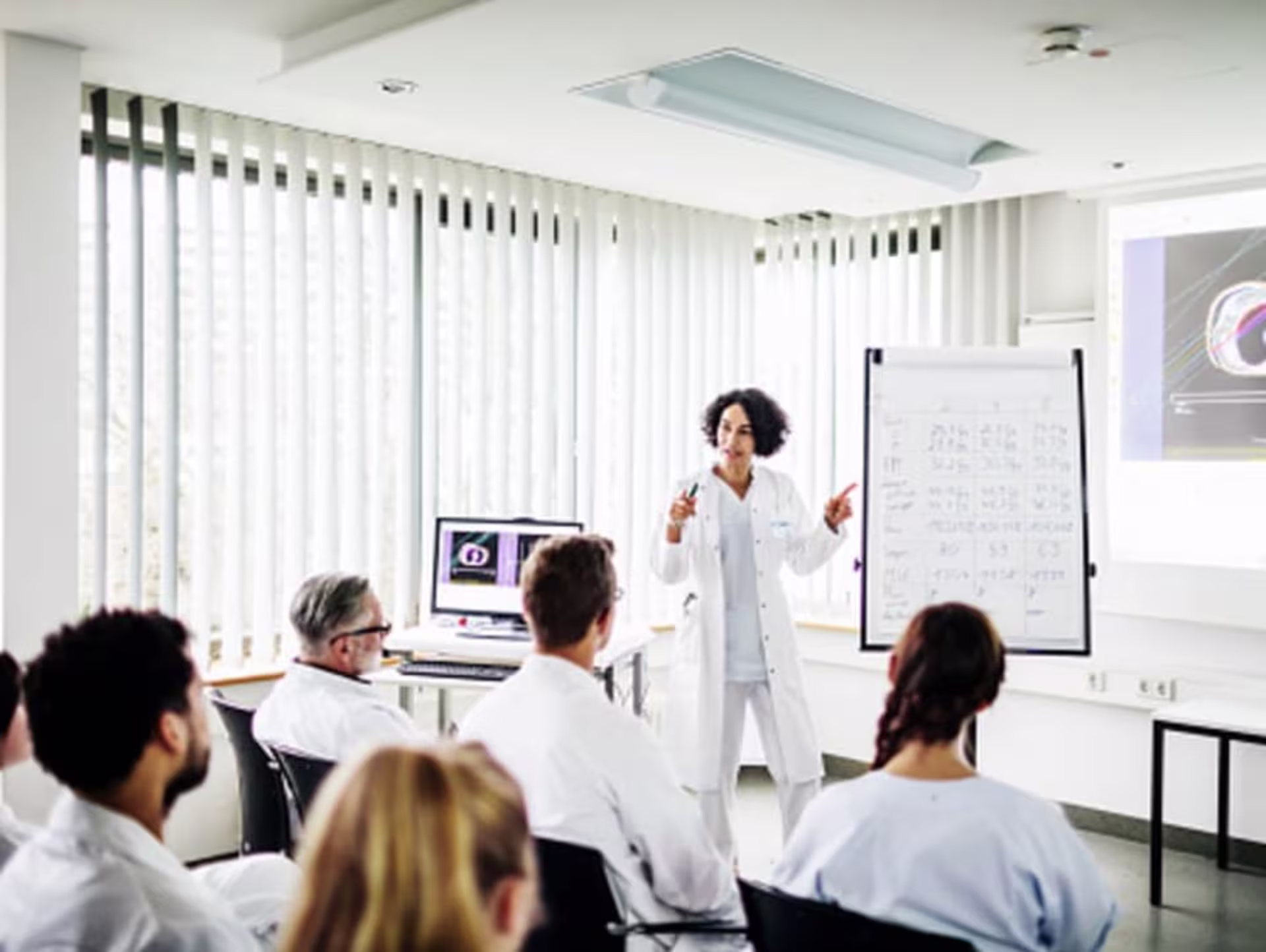 Medical instructor presenting to students in lab coats, discussing strategies for NCLEX exam preparation using visuals.