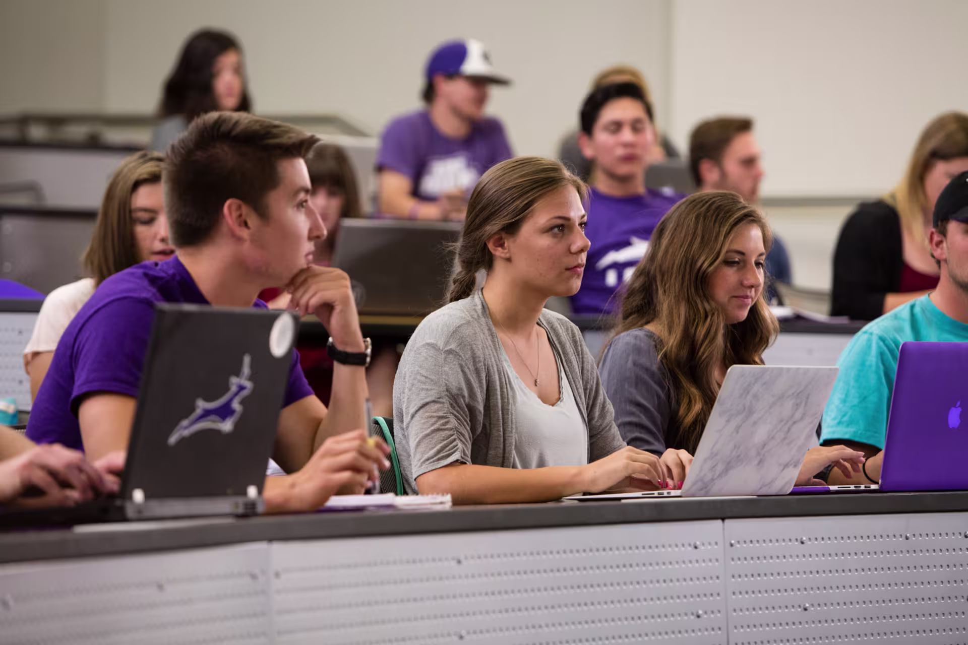 Male and female college students at desks in classroom with laptops.