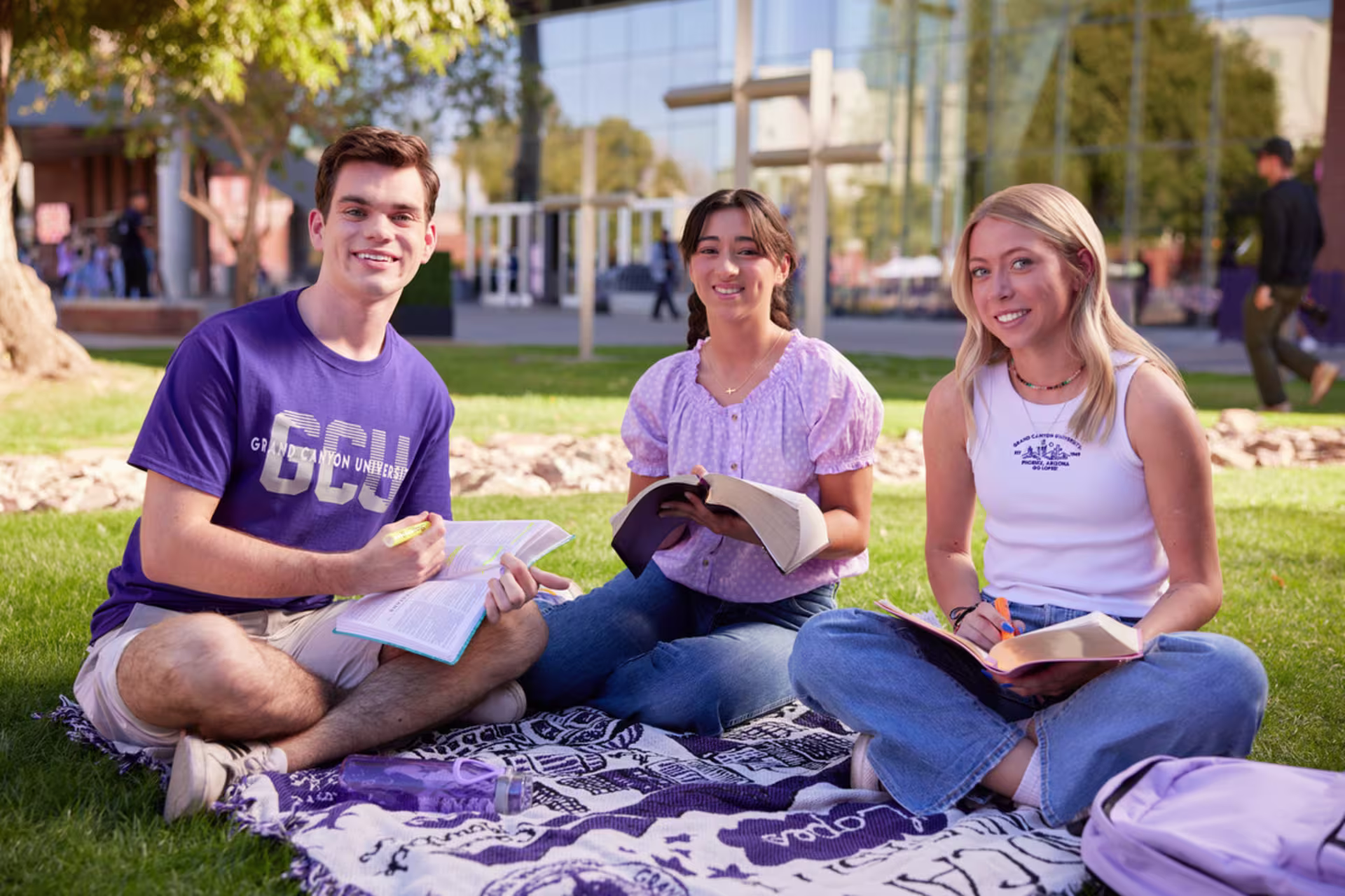 Group of three GCU students studying outside together on a blanket on the grass.