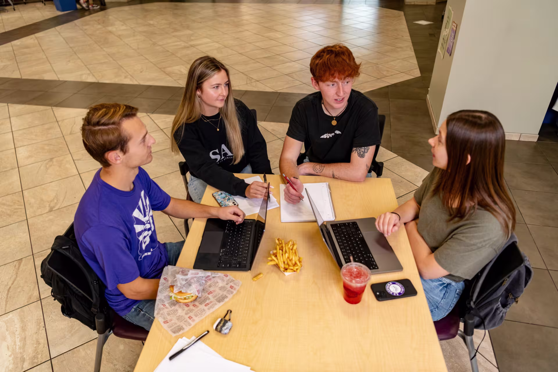Group of high school dual enrollment students doing homework online and eating together.