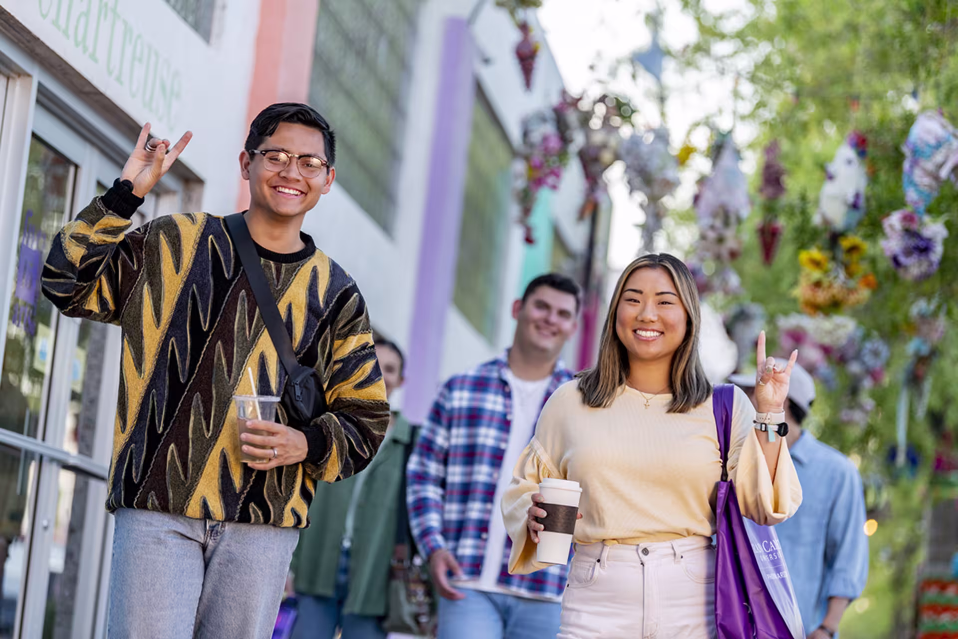 Group of GCU students walking around the outside of campus smiling and throwing up Lopes signs.