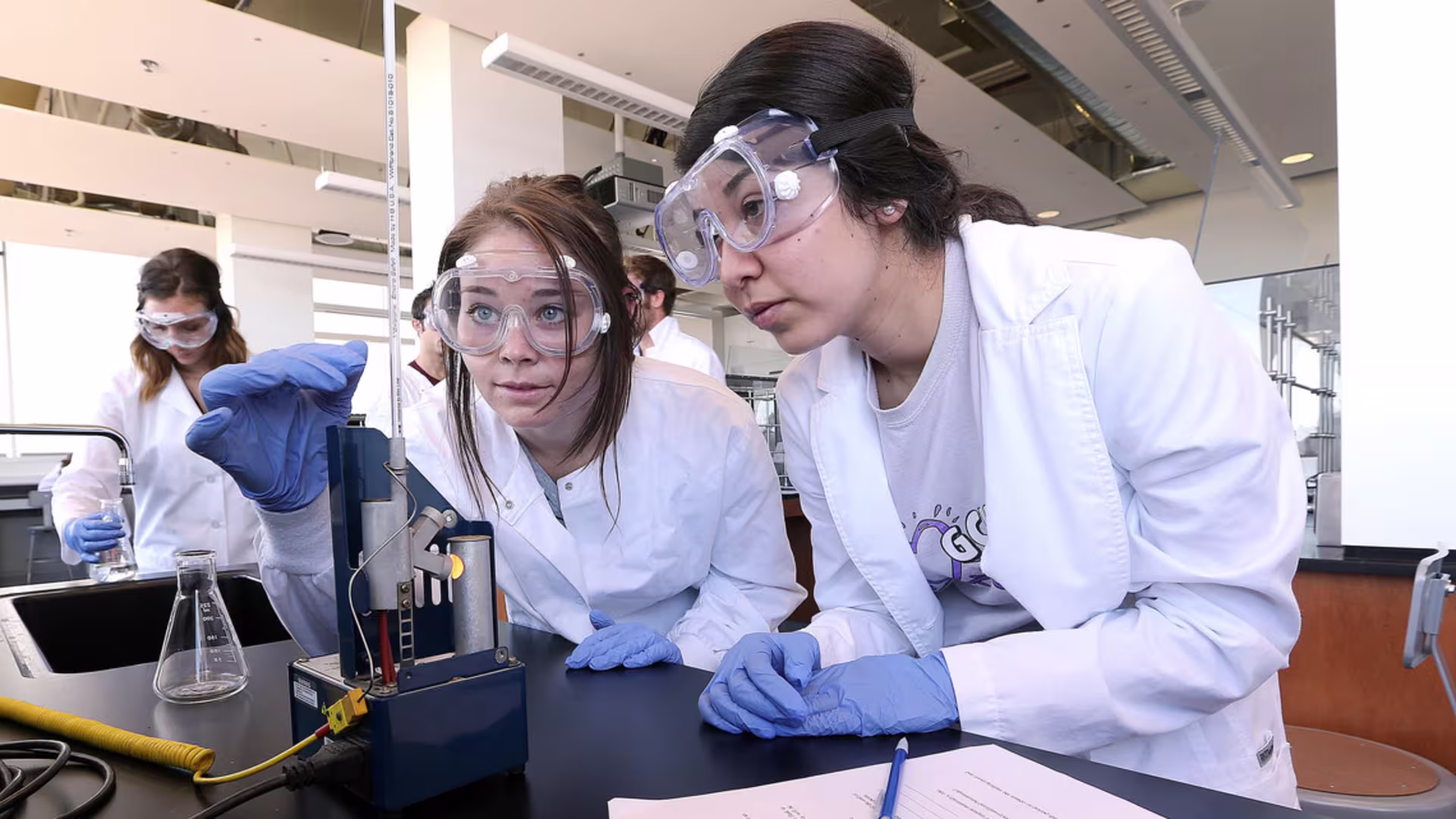two girls in ppe look closely at thermometer during chemistry lab