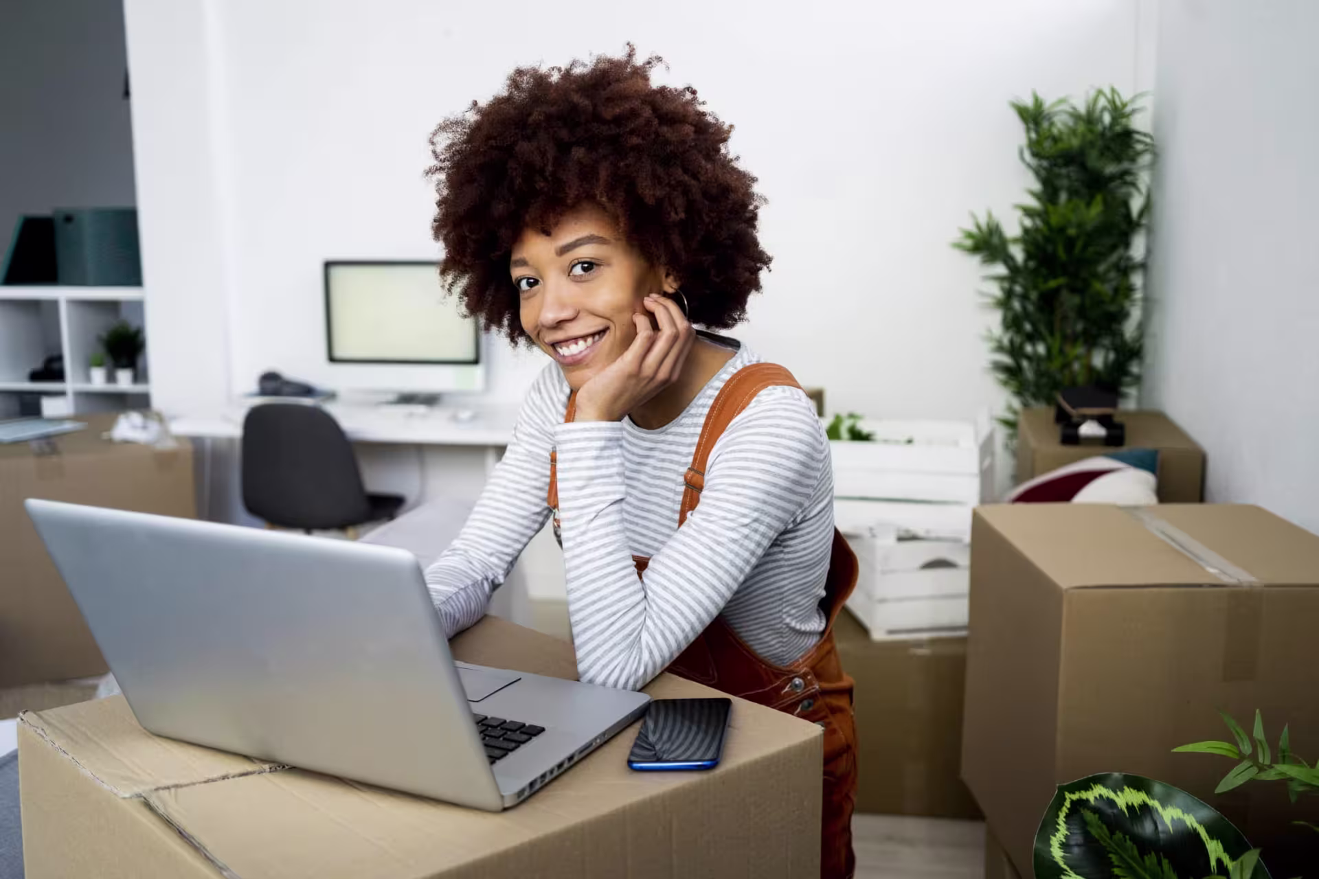 Student working on a laptop surrounded by moving boxes, shipping, logistics, and studying for the BS in Supply Chain and Logistics Management program.