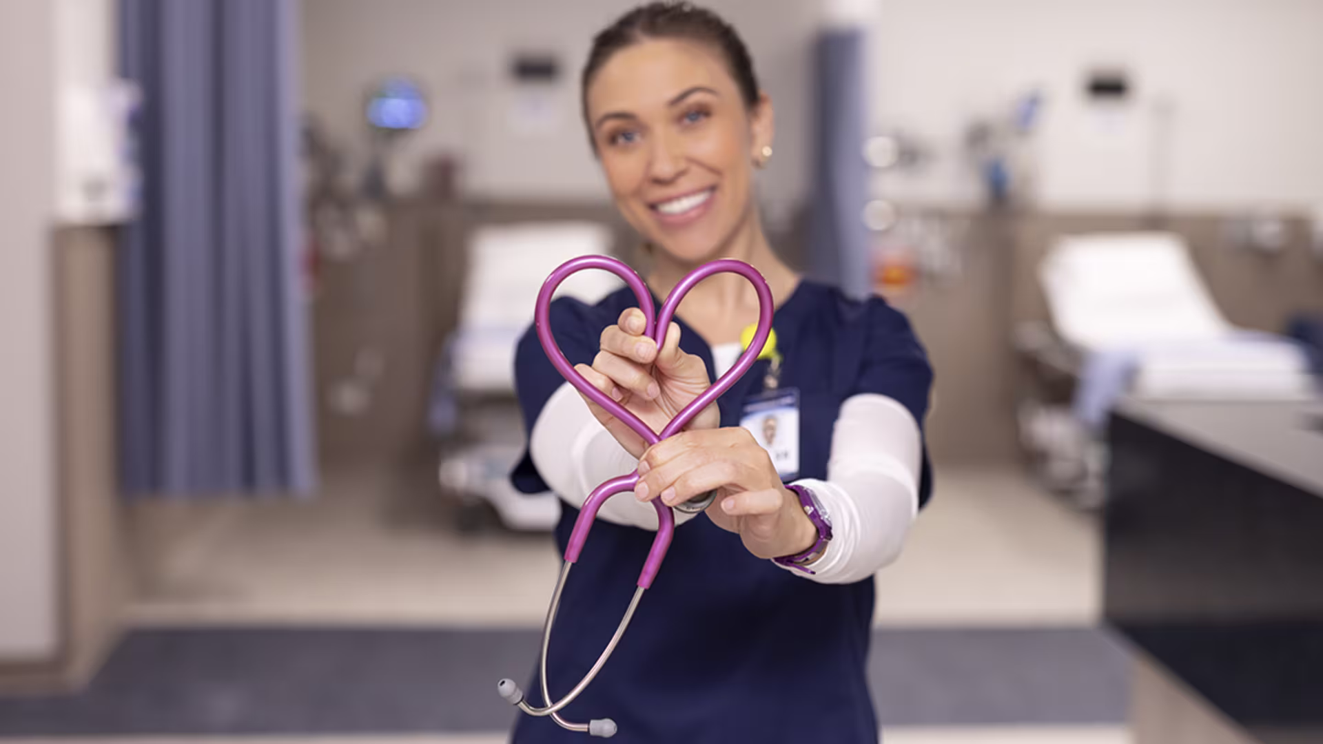 Female CON student making heart with pink stethoscope and smiling at camera
